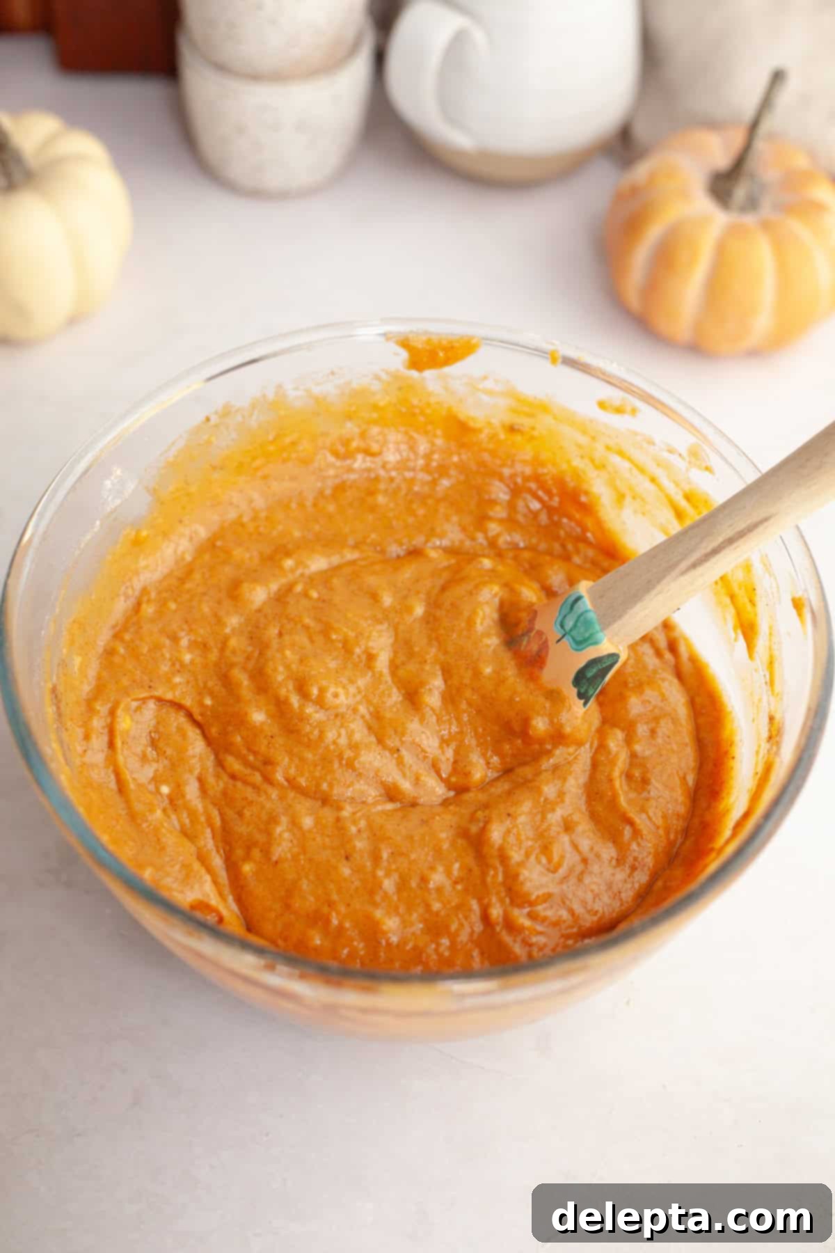 One-Bowl Pumpkin Sour Cream Muffins 5 Thick, vibrant pumpkin muffin batter folded gently with a rubber spatula in a glass bowl, ready for baking.