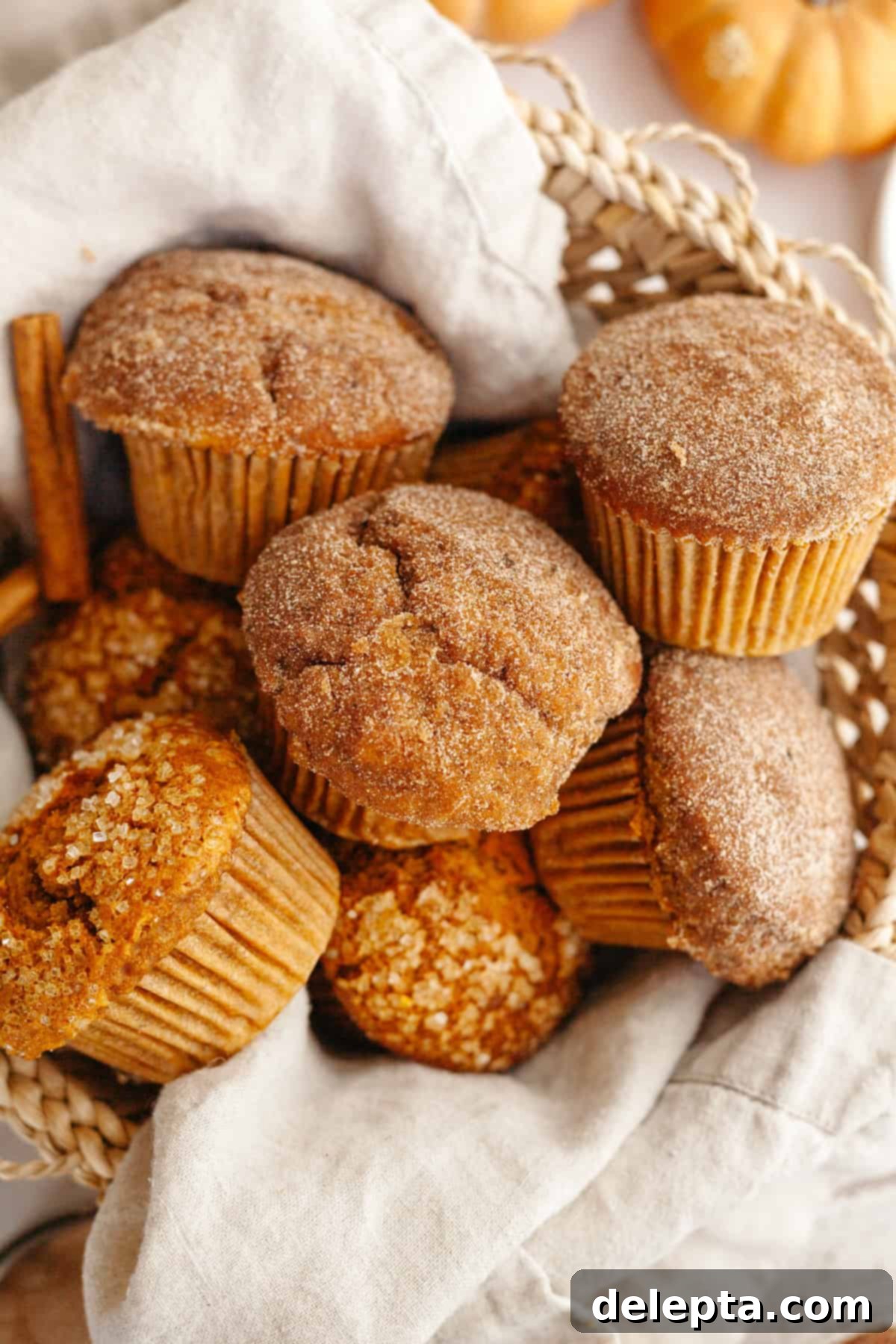 One-Bowl Pumpkin Sour Cream Muffins 8 A charming basket overflowing with freshly baked pumpkin sour cream muffins, each glistening with a sparkling sugar topping.