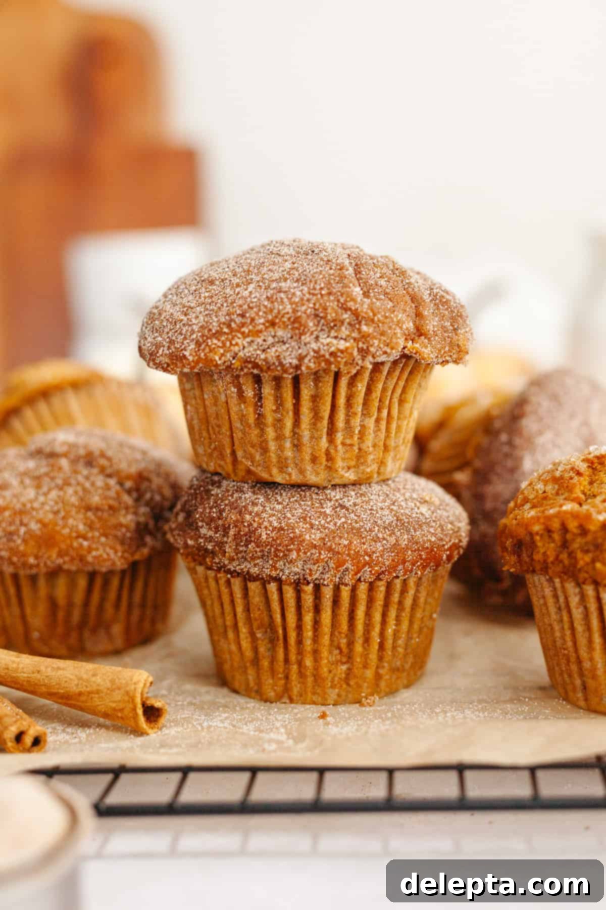 One-Bowl Pumpkin Sour Cream Muffins 9 A delightful stack of two pumpkin sour cream muffins, generously covered in a shimmering sugar topping, evoking autumn warmth.