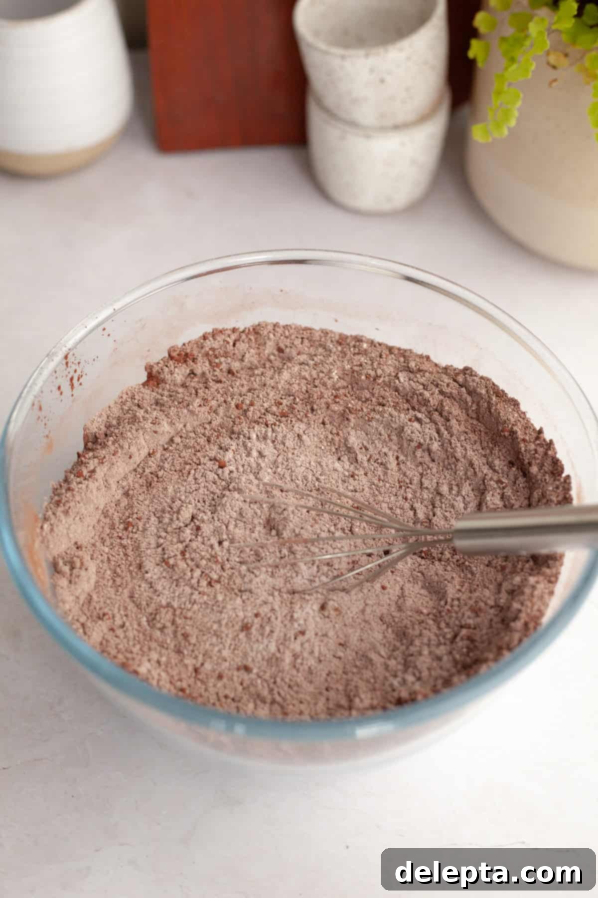 Easy Chocolate Sheet Cake 4 Flour and cocoa powder in a glass bowl with a whisk, illustrating the dry ingredients being combined.