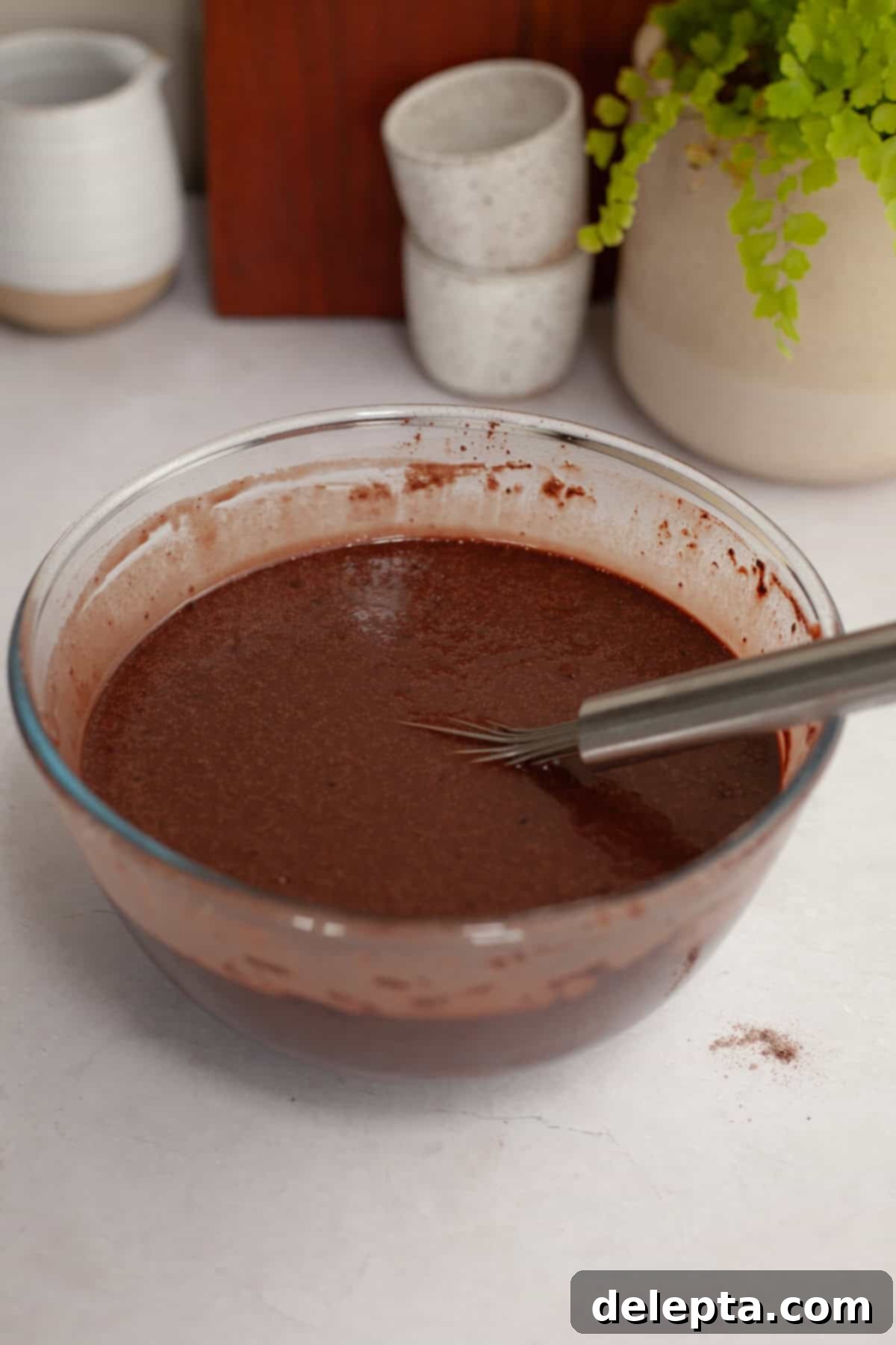 Easy Chocolate Sheet Cake 6 Chocolate cake batter in a glass bowl with a whisk, after hot water has been added, showing a very liquid consistency.