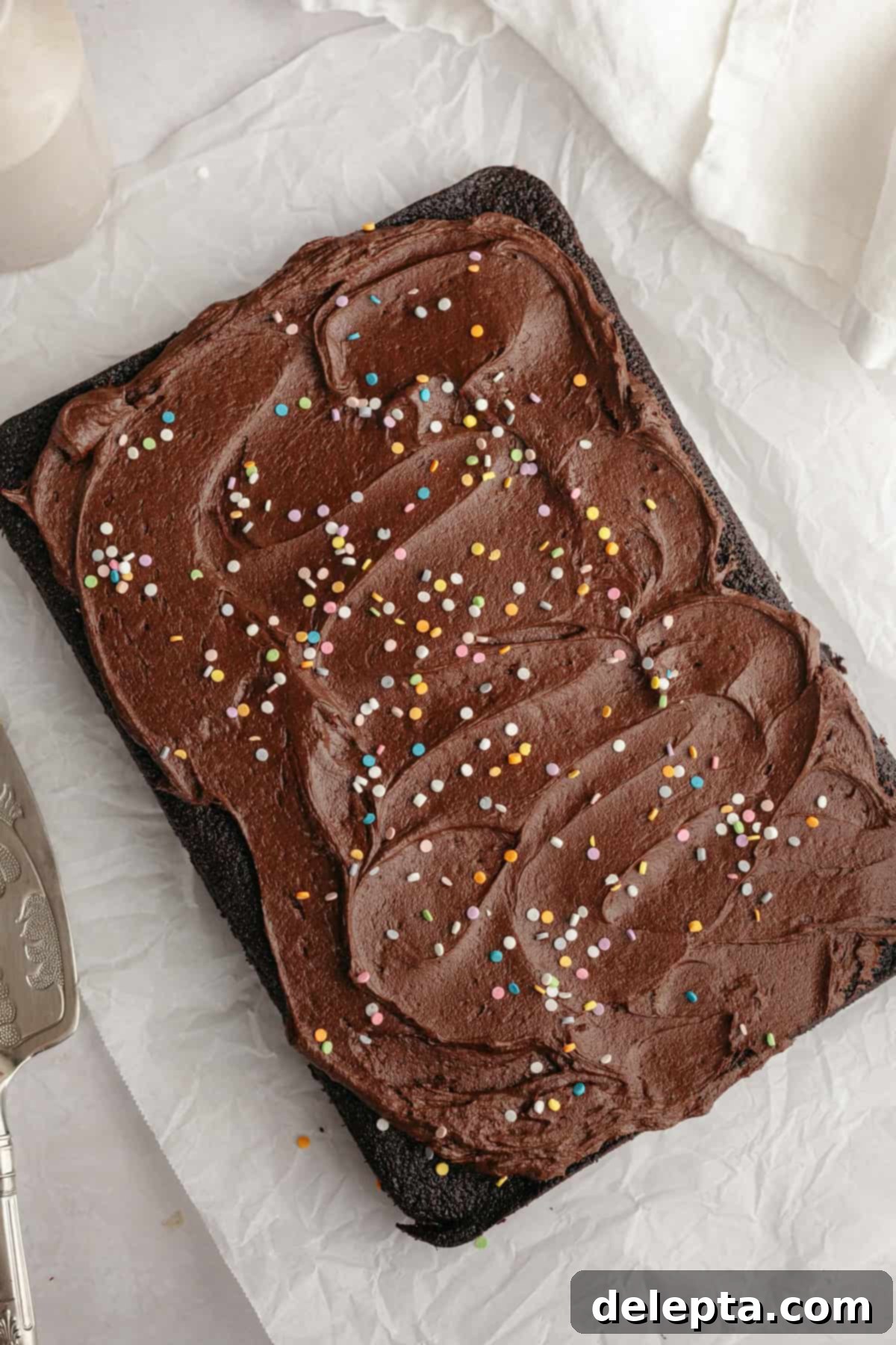 Easy Chocolate Sheet Cake 8 Chocolate sheet cake with chocolate frosting and rainbow sprinkles on parchment paper, ready to be cut.