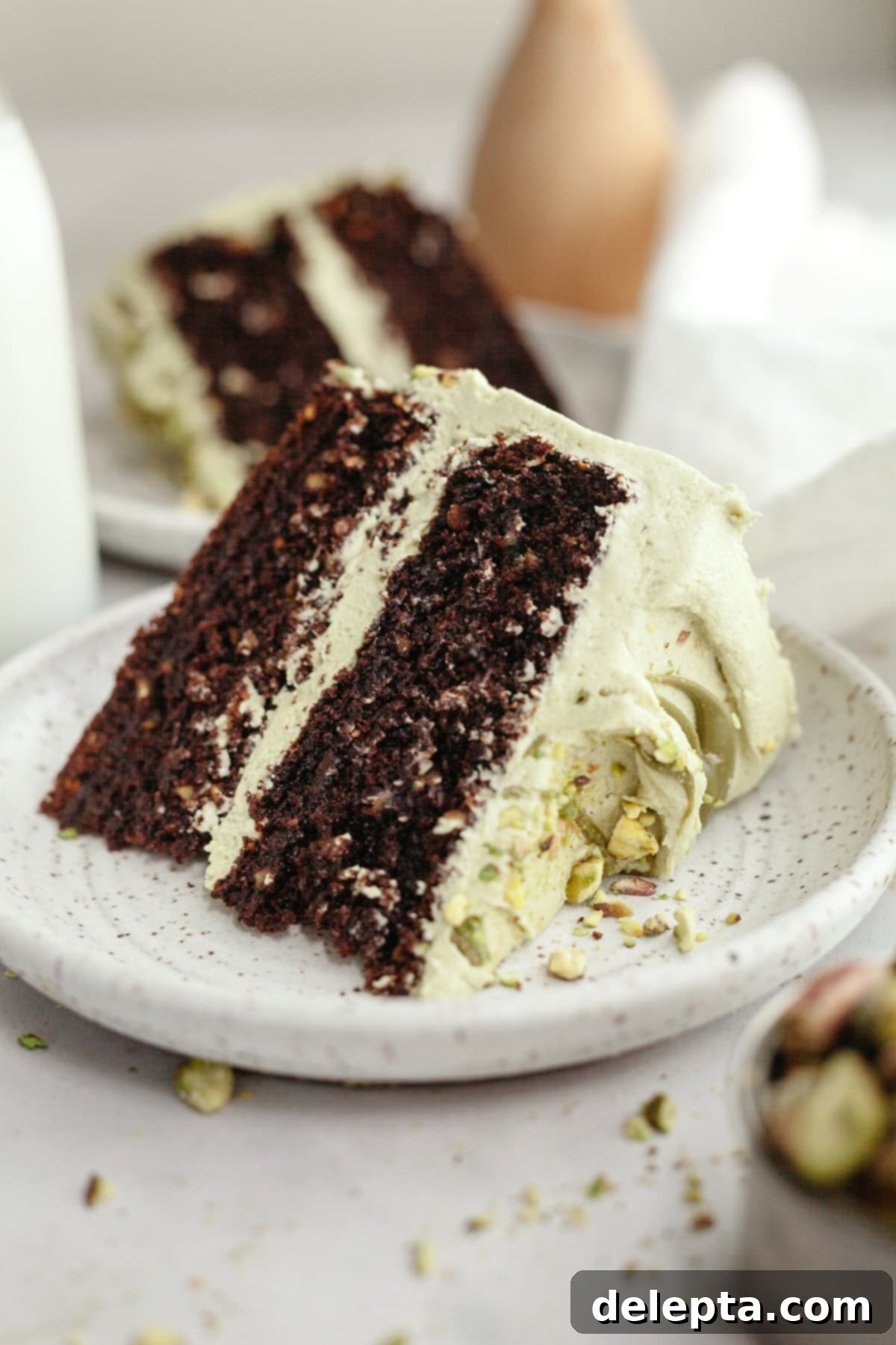 Decadent Chocolate Pistachio Dream Cake 2 A slice of pistachio chocolate cake on a small plate, beautifully frosted and garnished.