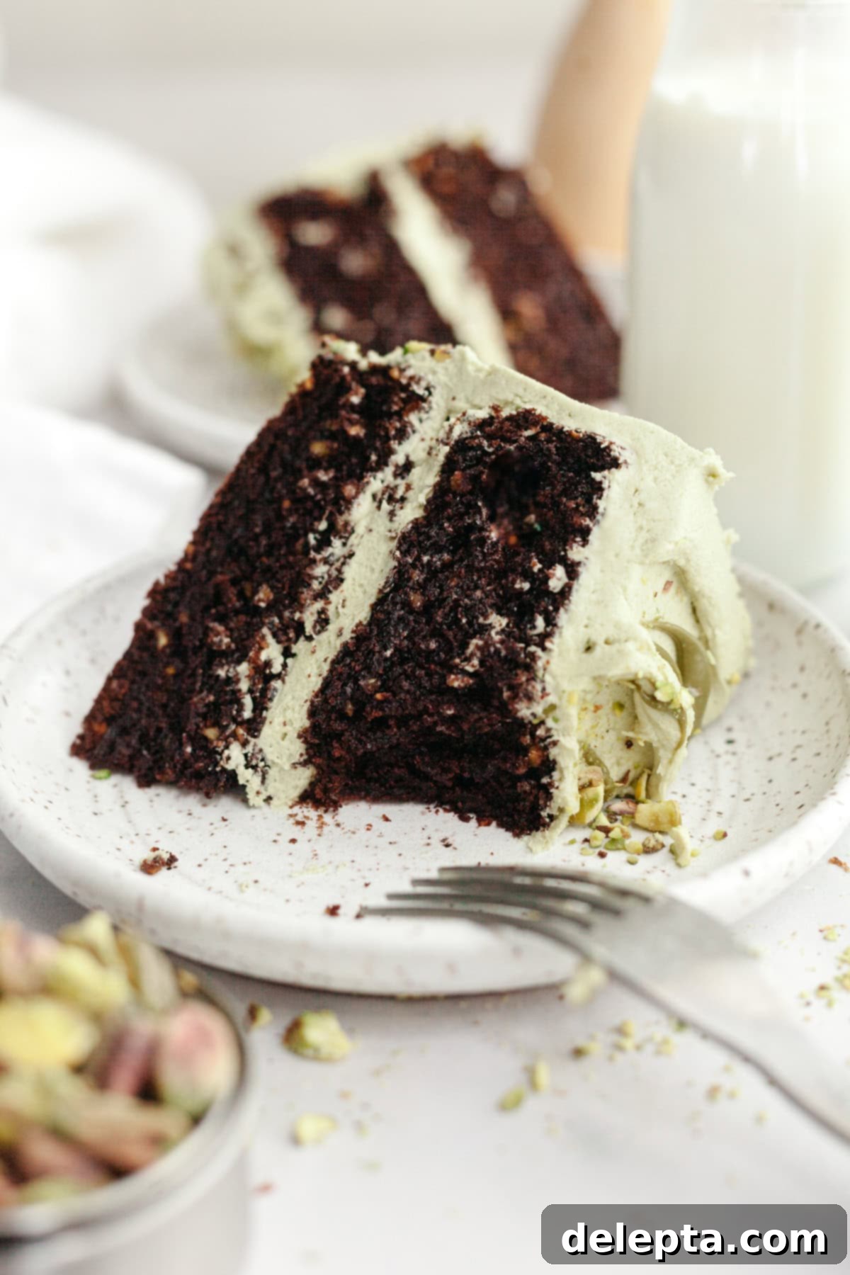 Decadent Chocolate Pistachio Dream Cake 11 A close-up slice of pistachio chocolate cake on a small plate, showing the texture of the cake and frosting.
