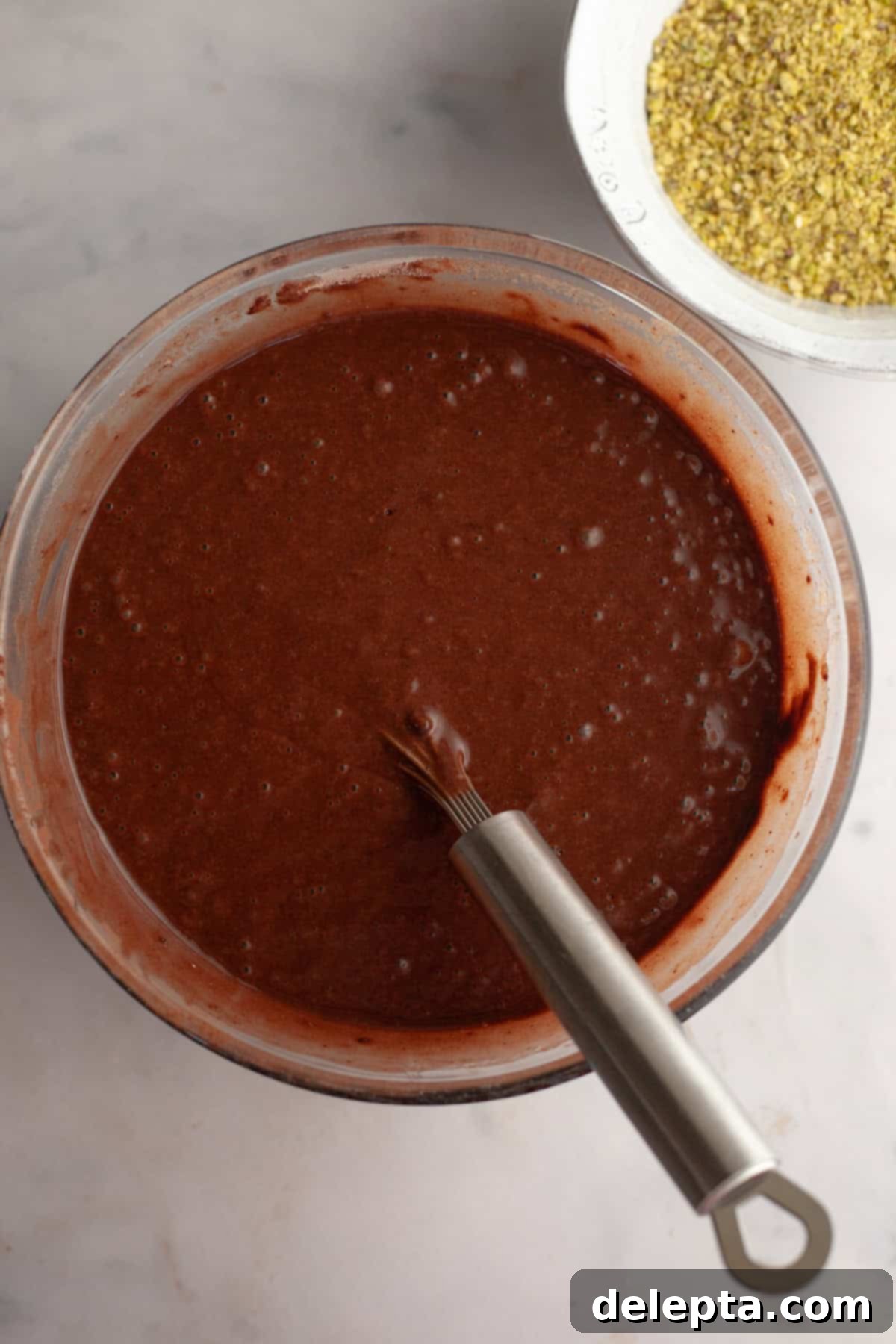 Decadent Chocolate Pistachio Dream Cake 5 Chocolate cake batter with a silver whisk in a glass bowl, after wet and dry ingredients are combined.