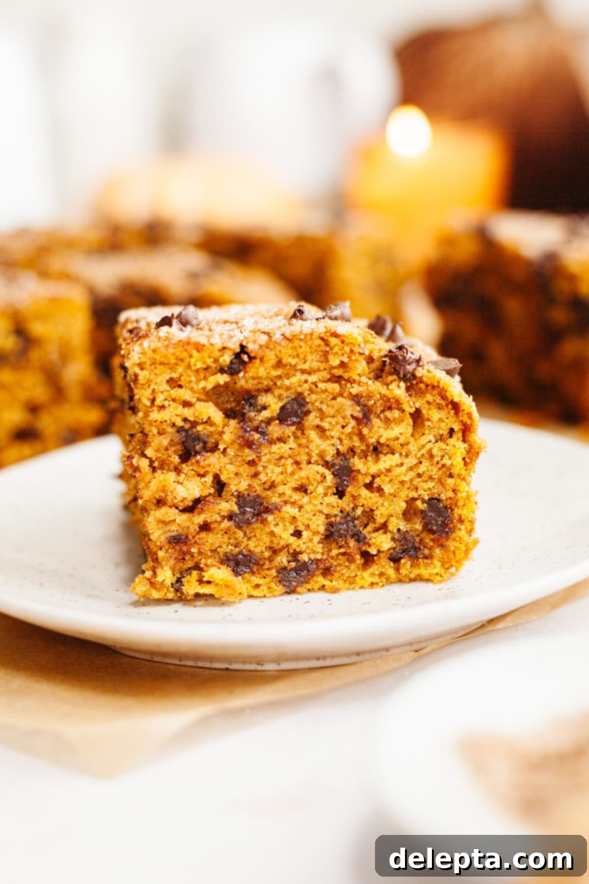 Easy One-Bowl Chocolate Chip Pumpkin Cake 2 A close up of a square slice of pumpkin chocolate chip cake on a small plate, showcasing its moist texture and mini chocolate chips.