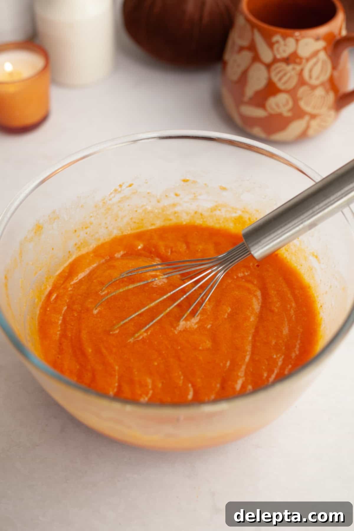 Easy One-Bowl Chocolate Chip Pumpkin Cake 4 Pumpkin cake batter in a glass bowl with a whisk, showing the smooth, combined wet ingredients.