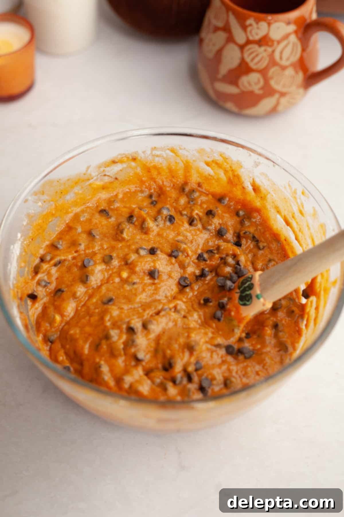 Easy One-Bowl Chocolate Chip Pumpkin Cake 6 Pumpkin chocolate chip cake batter in a glass bowl with a rubber spatula, showing the mini chocolate chips folded in.