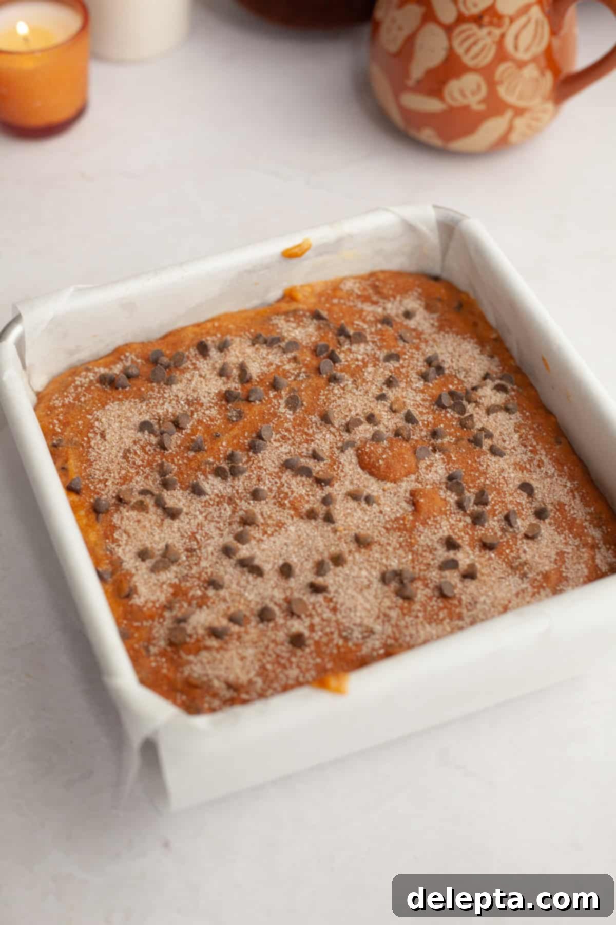 Easy One-Bowl Chocolate Chip Pumpkin Cake 7 Unbaked pumpkin chocolate chip cake in a square pan, topped with pumpkin spice sugar before baking.