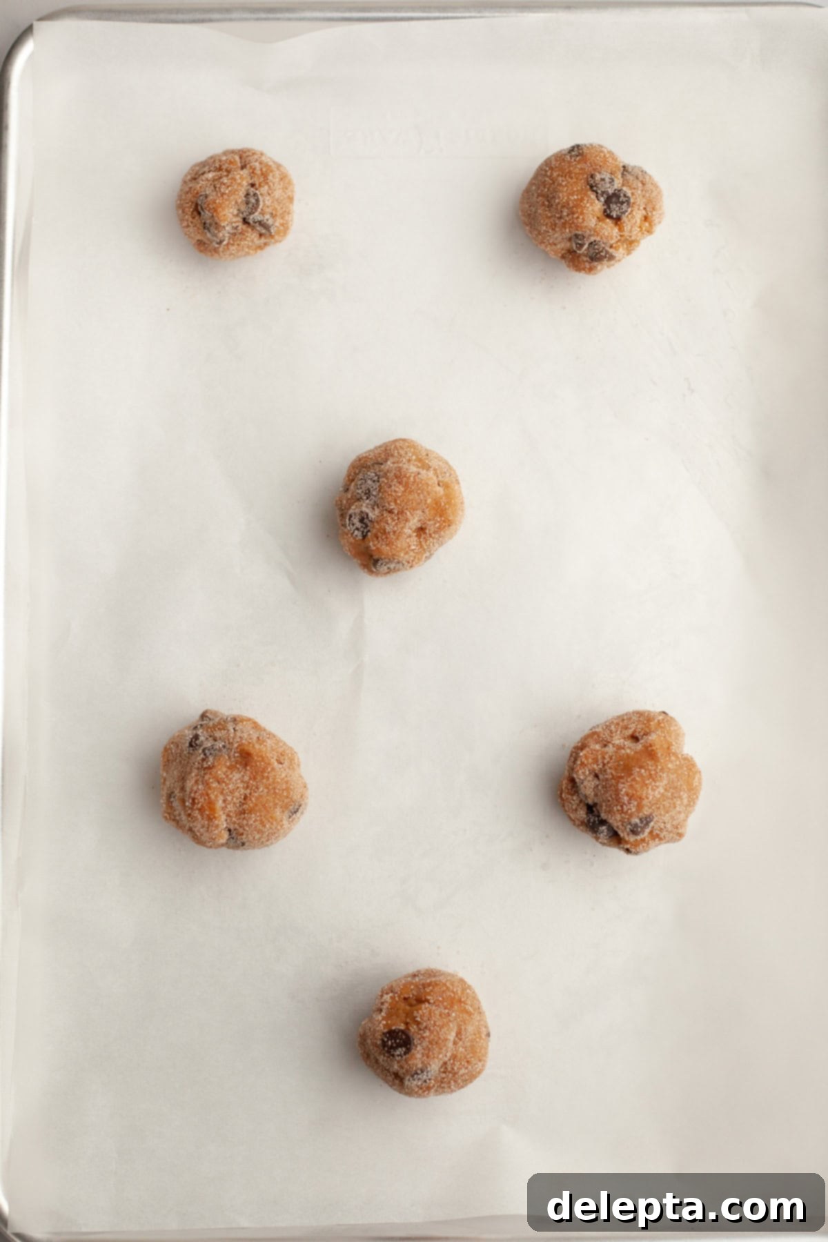 Nutty Brown Butter Pumpkin Chocolate Chip Cookies 9 Cookie dough balls rolled in sugar on parchment paper on a baking sheet.