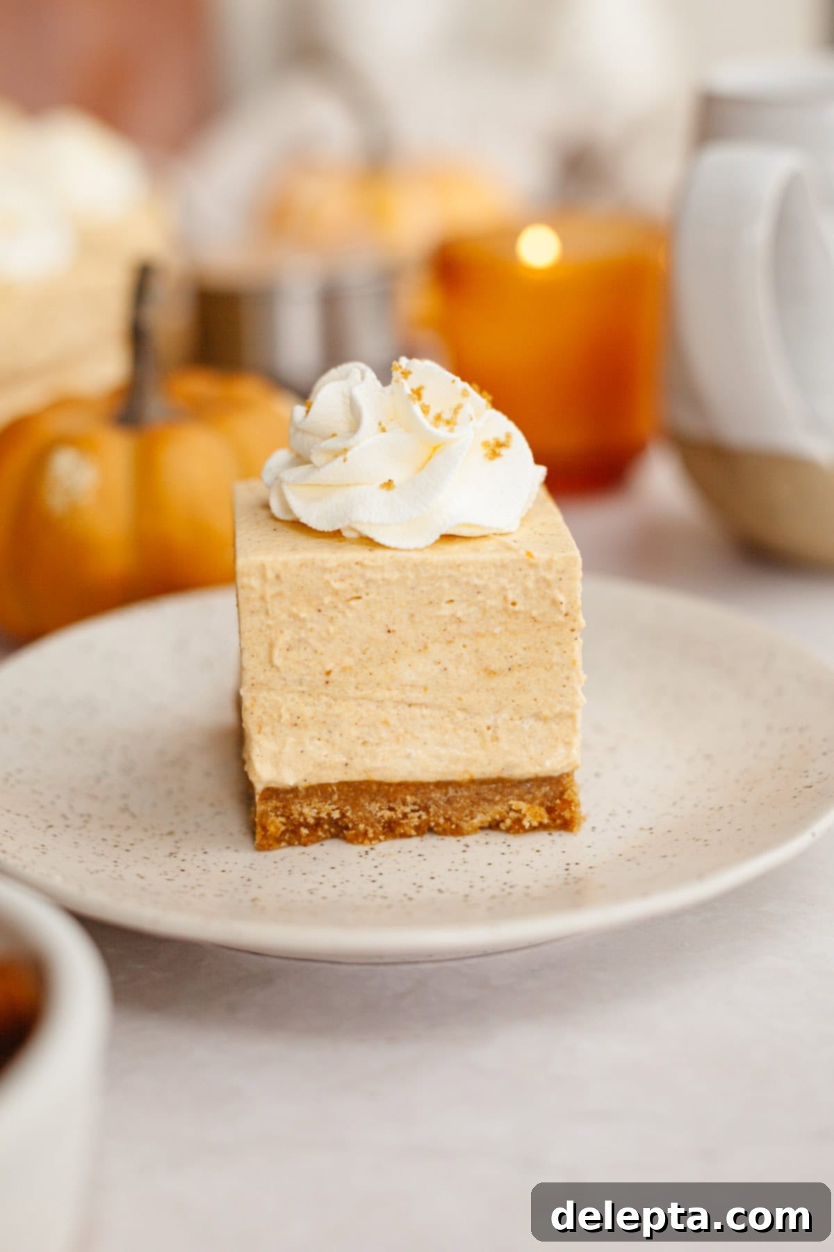 Spiced No-Bake Pumpkin Cheesecake Bars 2 A close up of no bake pumpkin cheesecake bars topped with whipped cream on a small plate, ready to be enjoyed.