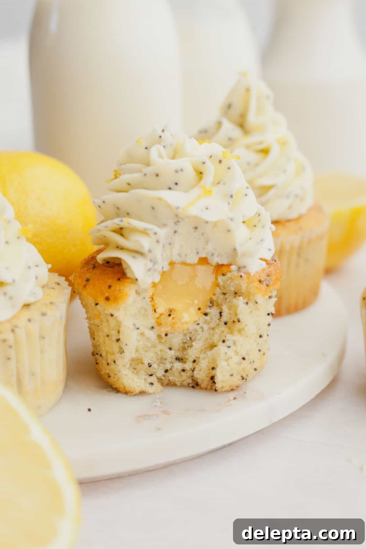 Sunshine Lemon Poppy Seed Cupcakes 2 A perfectly baked lemon poppy seed cupcake with a generous swirl of lemon frosting, and a small bite taken out to reveal a bright yellow lemon curd filling inside.