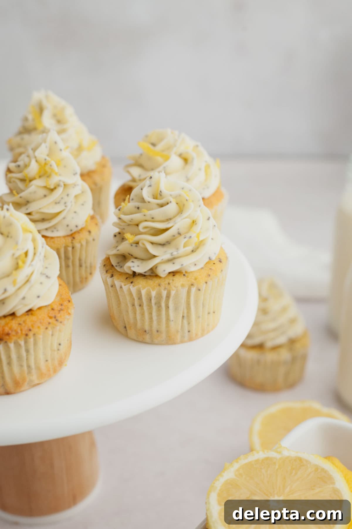 Sunshine Lemon Poppy Seed Cupcakes 11 Several beautifully frosted lemon poppy seed cupcakes arranged on a pristine white cake stand, ready to be served.