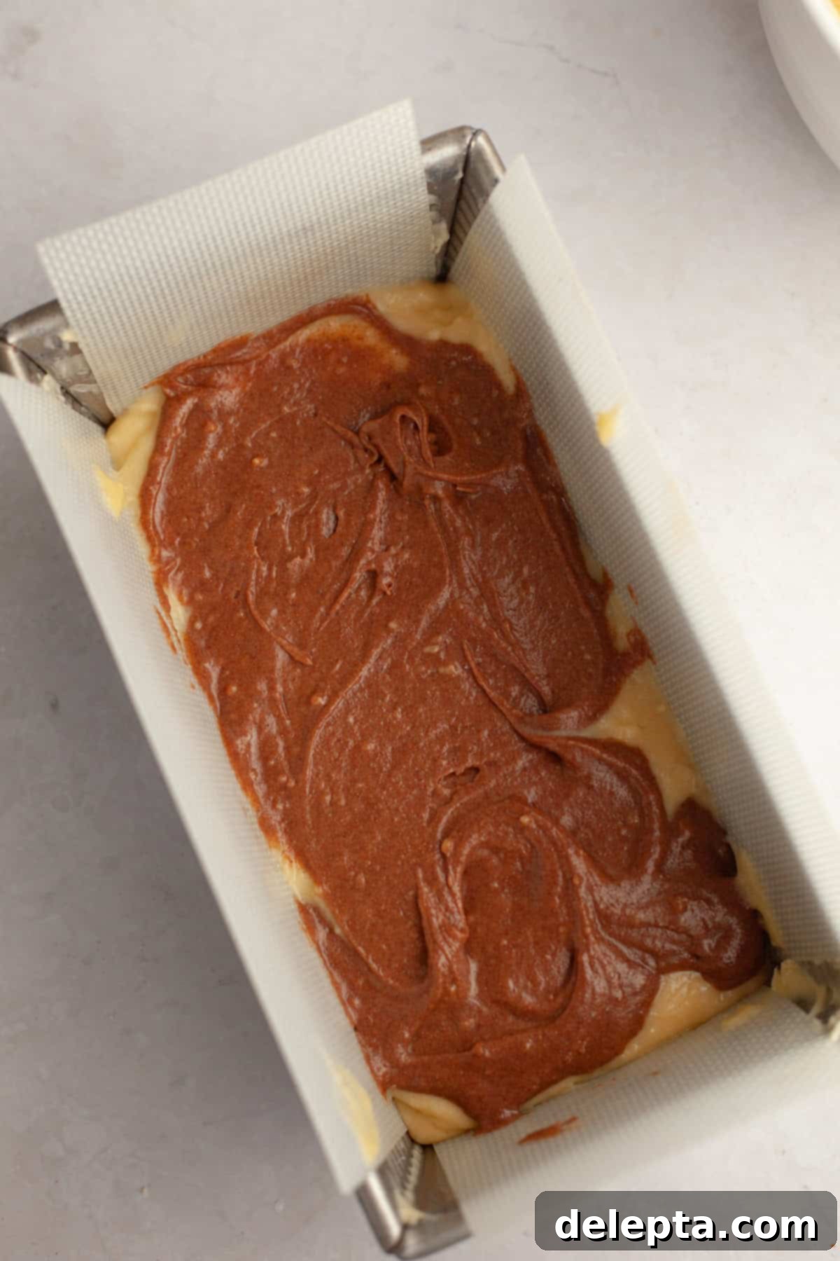 Velvet Cinnamon Pound Cake with Espresso Maple Glaze 8 A loaf pan half-filled with light yellow cake batter, with a layer of darker cinnamon batter spooned on top.