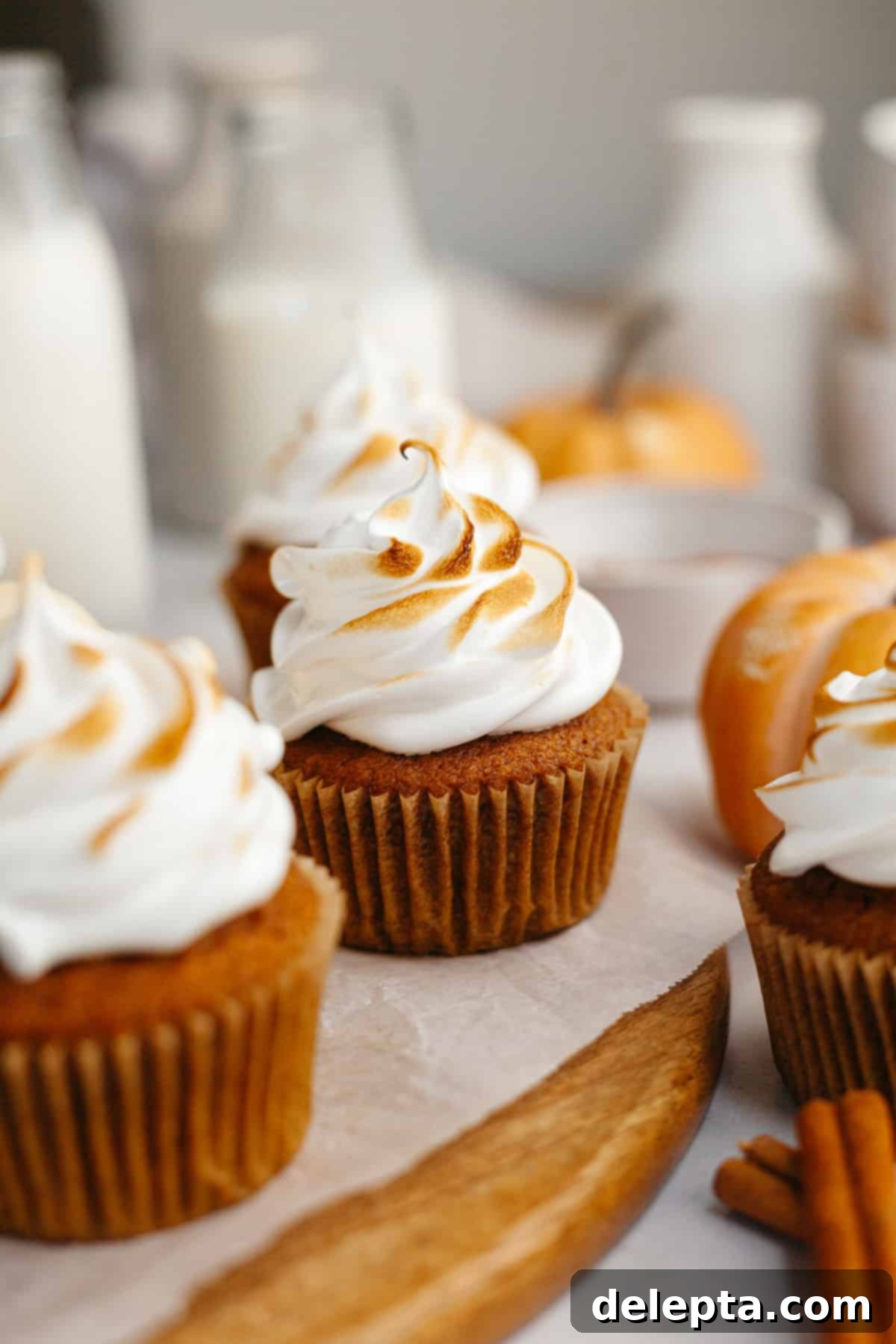 Spiced Pumpkin Cupcakes with Whipped Marshmallow Frosting 2 Delicious pumpkin cupcakes with toasted marshmallow frosting beautifully arranged on a rustic wooden board, perfect for fall celebrations.