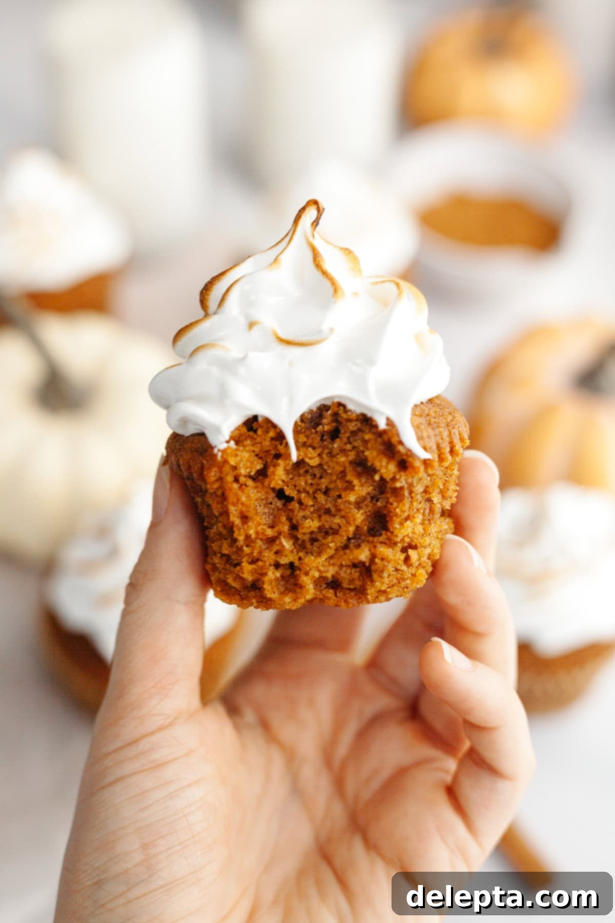 Spiced Pumpkin Cupcakes with Whipped Marshmallow Frosting 11 A hand holding a perfectly baked pumpkin cupcake with a bite taken out, showcasing the moist interior and toasted marshmallow frosting.