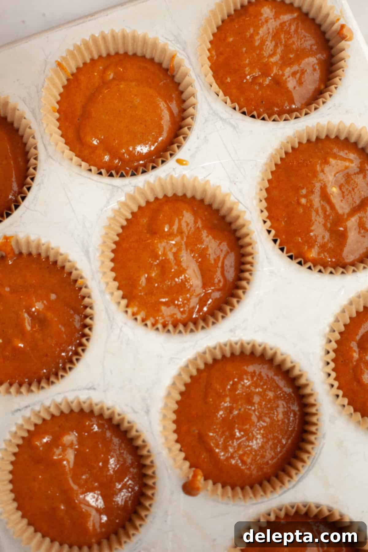 Spiced Pumpkin Cupcakes with Whipped Marshmallow Frosting 8 Unbaked pumpkin cupcakes with paper liners neatly arranged in a cupcake pan, ready for the oven.