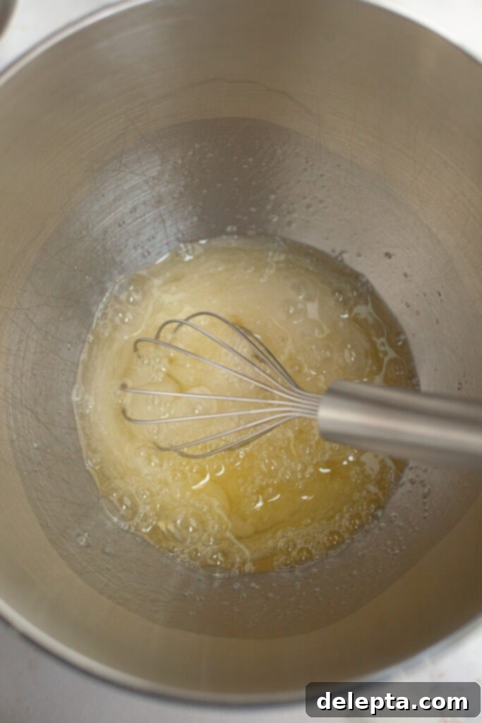 Fluffy Marshmallow Meringue Frosting 4 A metal mixing bowl filled with egg whites, granulated sugar, and cream of tartar, carefully positioned over a saucepan of simmering water for a double boiler setup.