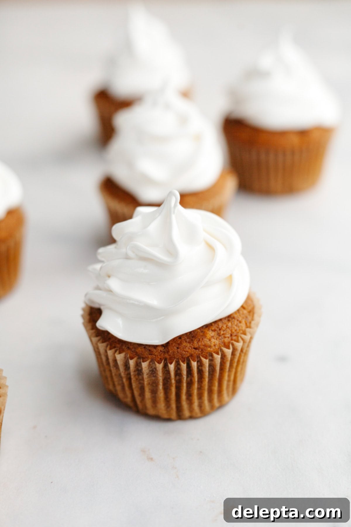 Fluffy Marshmallow Meringue Frosting 7 A trio of delicious pumpkin spice cupcakes, each adorned with a generous swirl of perfectly toasted marshmallow meringue frosting, presented elegantly.