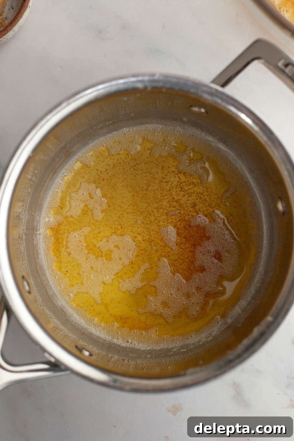 Decadent Brown Butter Pumpkin Pie with Gingersnap Perfection 6 A small saucepan on the stove containing golden brown butter with amber bits at the bottom, exuding a rich, nutty aroma.
