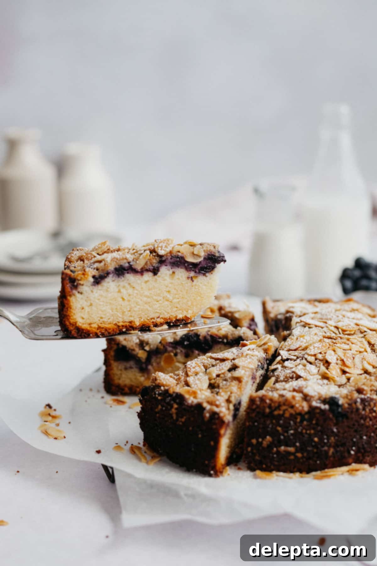 Sun-Kissed Blueberry Almond Lemon Cake 10 A beautiful blueberry almond lemon cake with one perfectly baked slice being gently lifted out by a cake server.