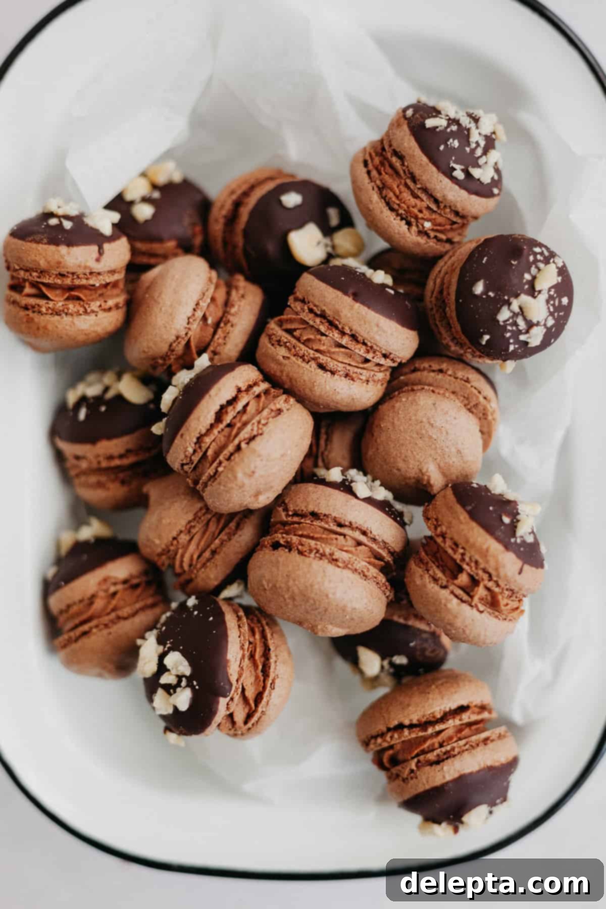 Decadent Nutella Macarons 2 Nutella macarons on parchment paper, showcasing their delicate feet and chocolate-hazelnut topping