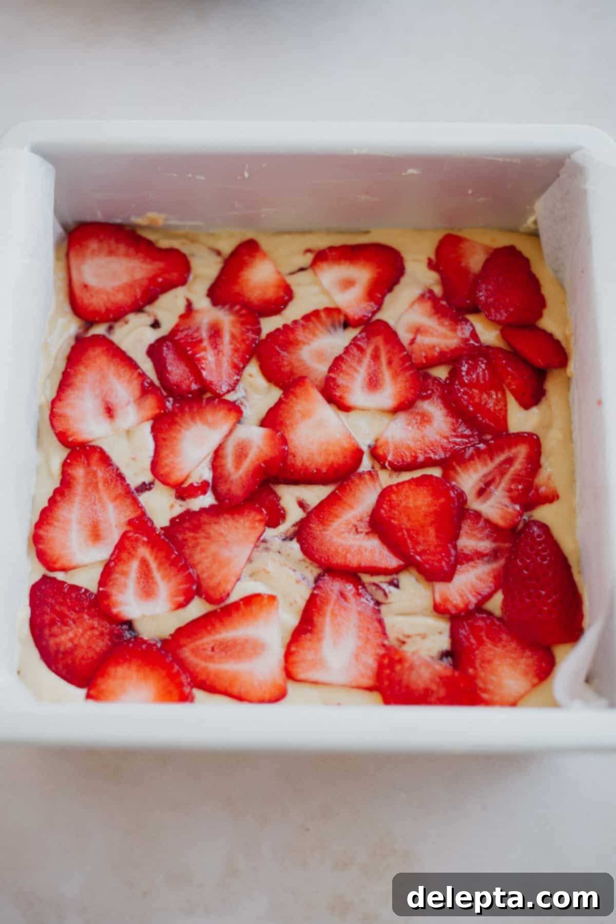Luscious Strawberry Crumb Cake 11 A cake pan with cake batter, the batter is topped with very thinly sliced strawberries.