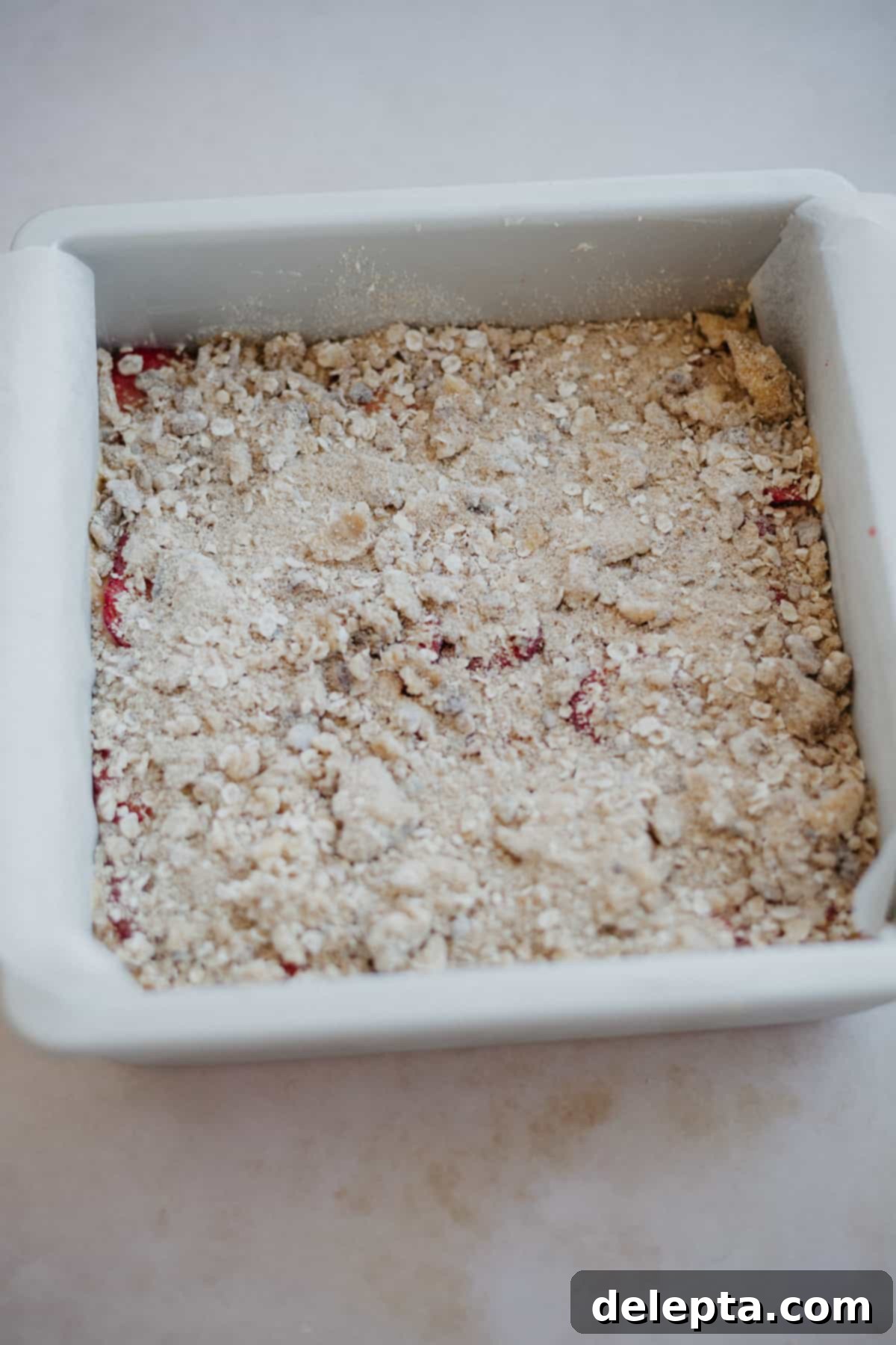 Luscious Strawberry Crumb Cake 12 A cake pan filled with cake batter then covered in an oat crumble topping
