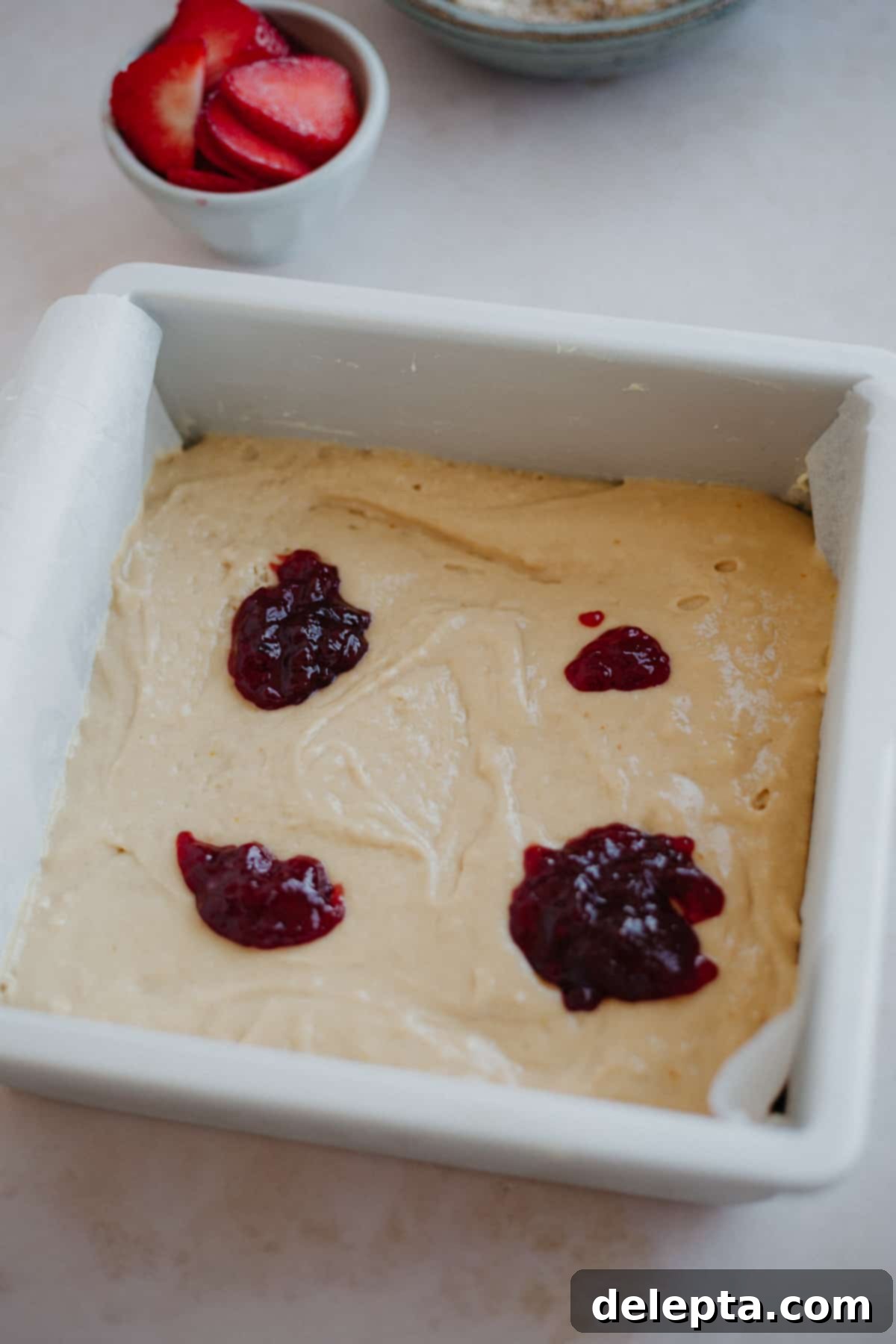 Luscious Strawberry Crumb Cake 9 A cake pan filled with cake batter and dollops of jam.
