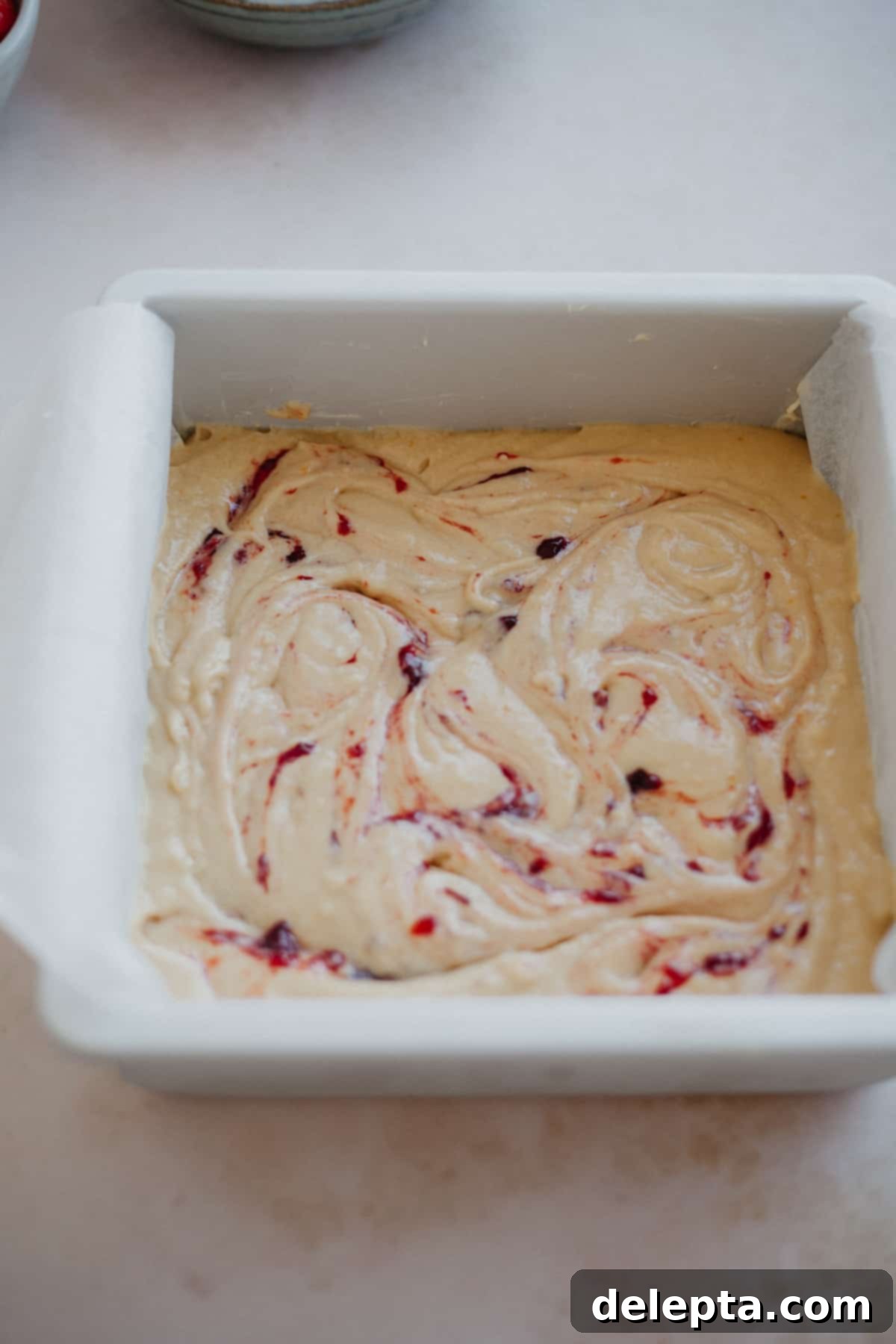 Luscious Strawberry Crumb Cake 10 A cake pan filled with cake batter and dollops of jam which has been swirled.