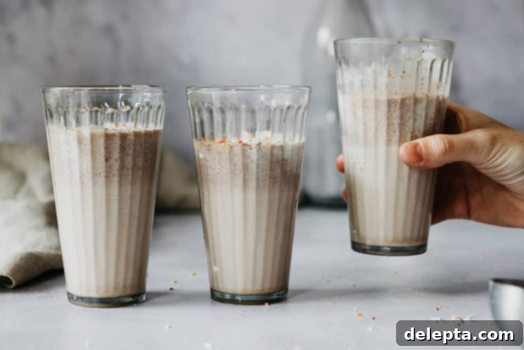 Frosty Funfetti Shakes 2 Three glasses filled with birthday cake milkshake, one is being picked up by a hand against a light background