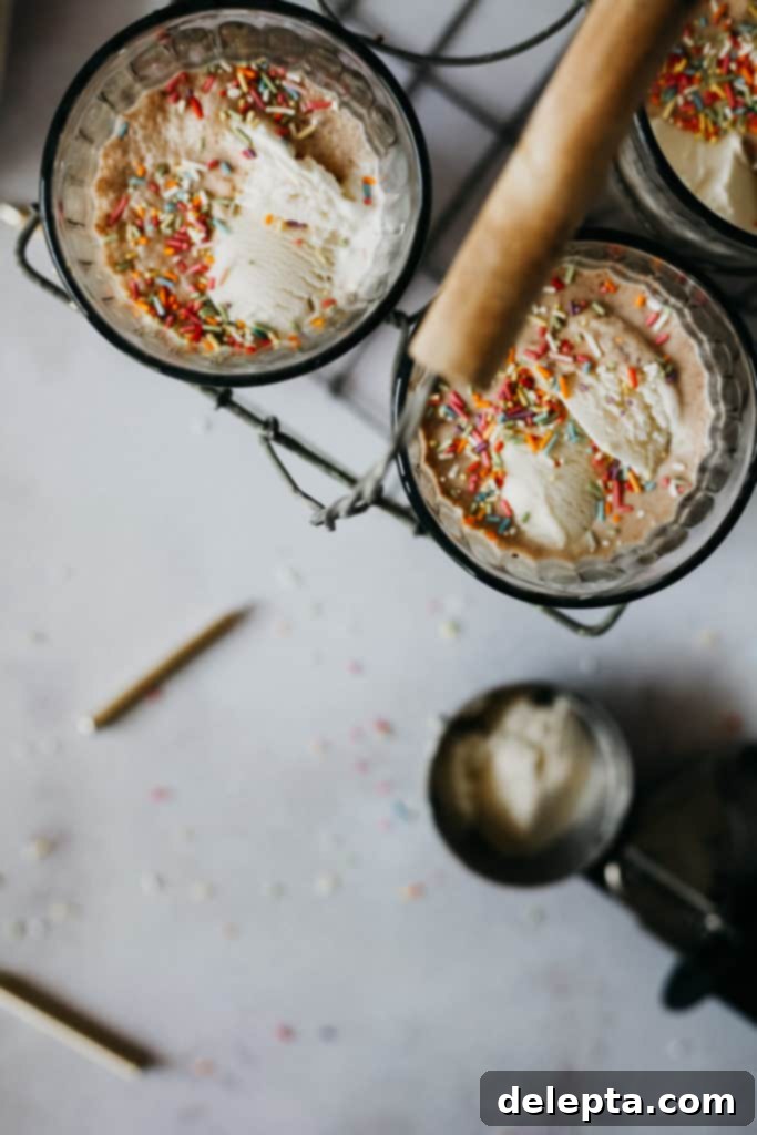 Frosty Funfetti Shakes 3 Bird's eye view of a single milkshake glass, with an ice cream scooper and sprinkles on a rustic wooden table
