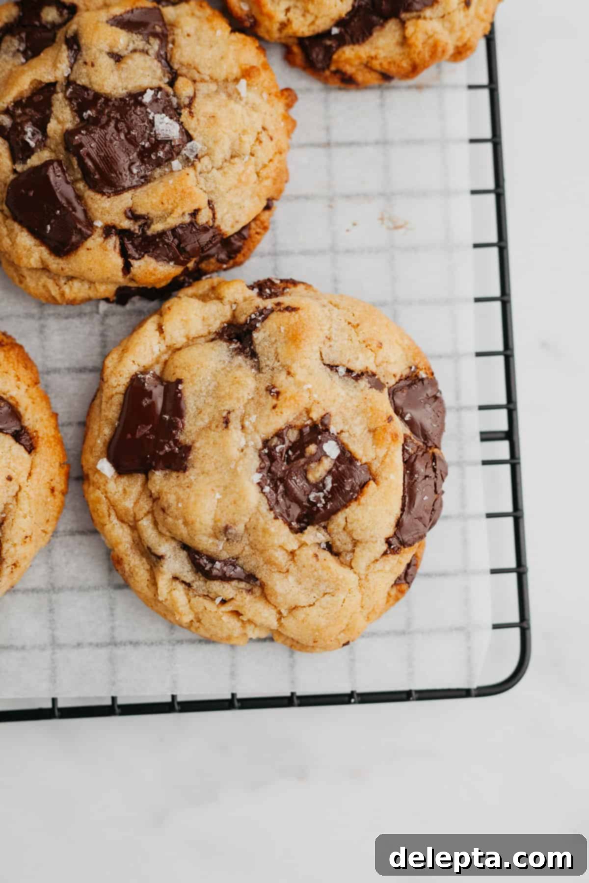 Miso Magic Brown Butter Chocolate Chip Cookies 2 A close up of a chocolate chunk cookie on parchment paper, showing melted chocolate puddles.