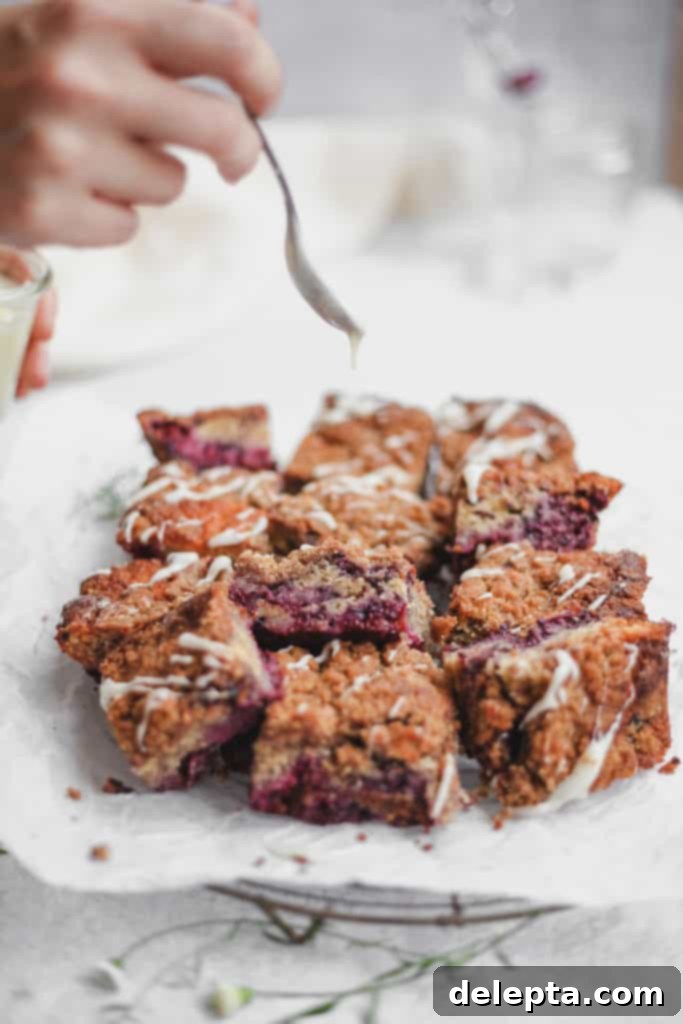 Blackberry Streusel Buckle with Cream Cheese Drizzle 2 Cut blackberry buckle bars being drizzled with cream cheese glaze, showing off the fluffy cake and juicy berries inside.