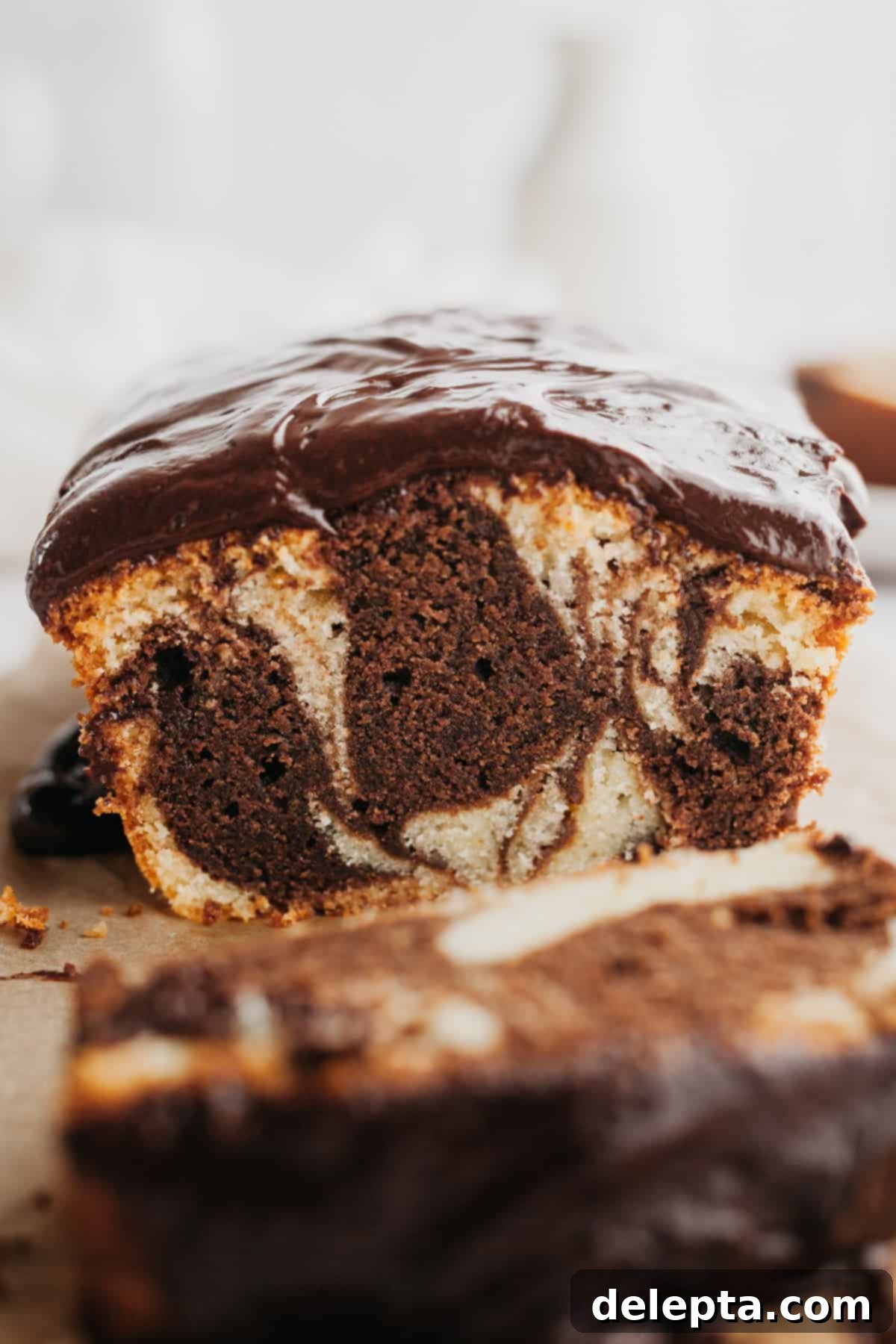 Elegant Swirl Loaf 2 A close up of a marble loaf cake covered with chocolate ganache, showcasing the beautiful swirl pattern when sliced.