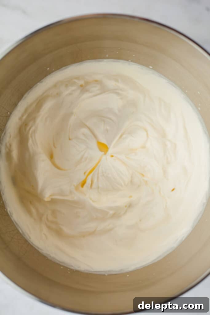 Blonde Oreo Cheesecake 6 A large silver mixing bowl filled with perfectly whipped heavy cream, displaying stiff peaks.