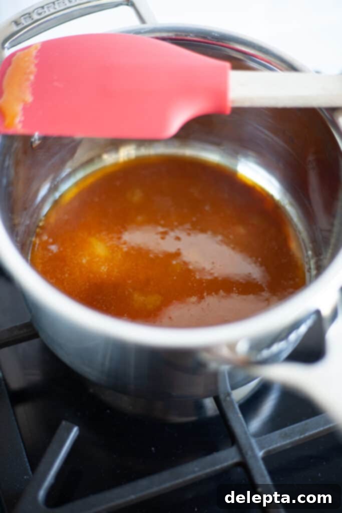 Sea Salt Caramel Macarons 12 A small saucepan on the stove, containing bubbling, dark amber colored caramel, signifying it's almost done.