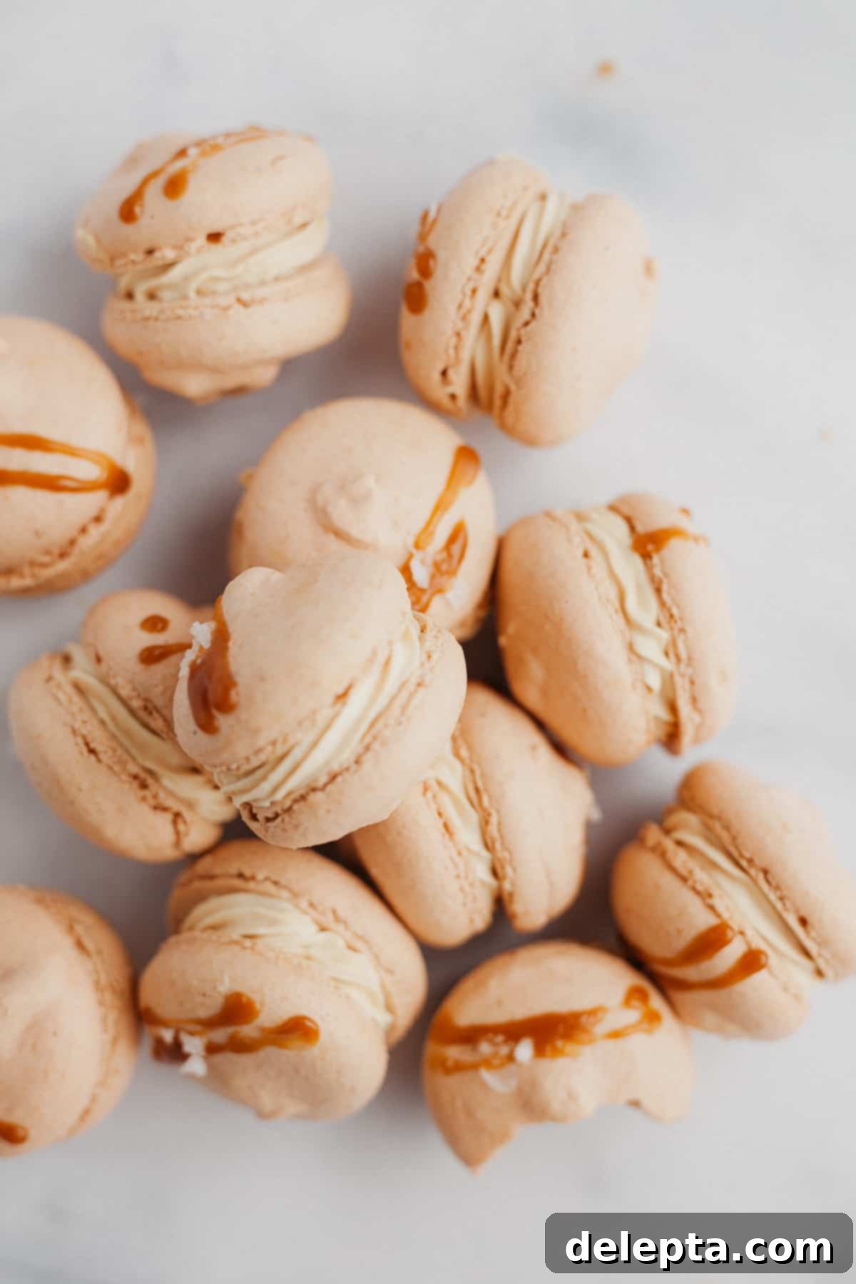Sea Salt Caramel Macarons 19 Approximately ten beautifully assembled salted caramel macarons, laid on their sides on a elegant marble counter, highlighting their delicious filling.