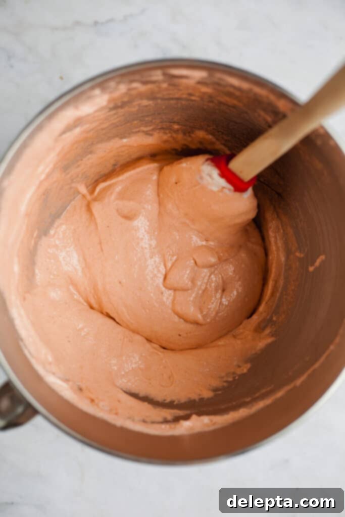 Sea Salt Caramel Macarons 8 A silver mixing bowl with macaron batter being gently folded with a rubber spatula, showing its developing consistency.