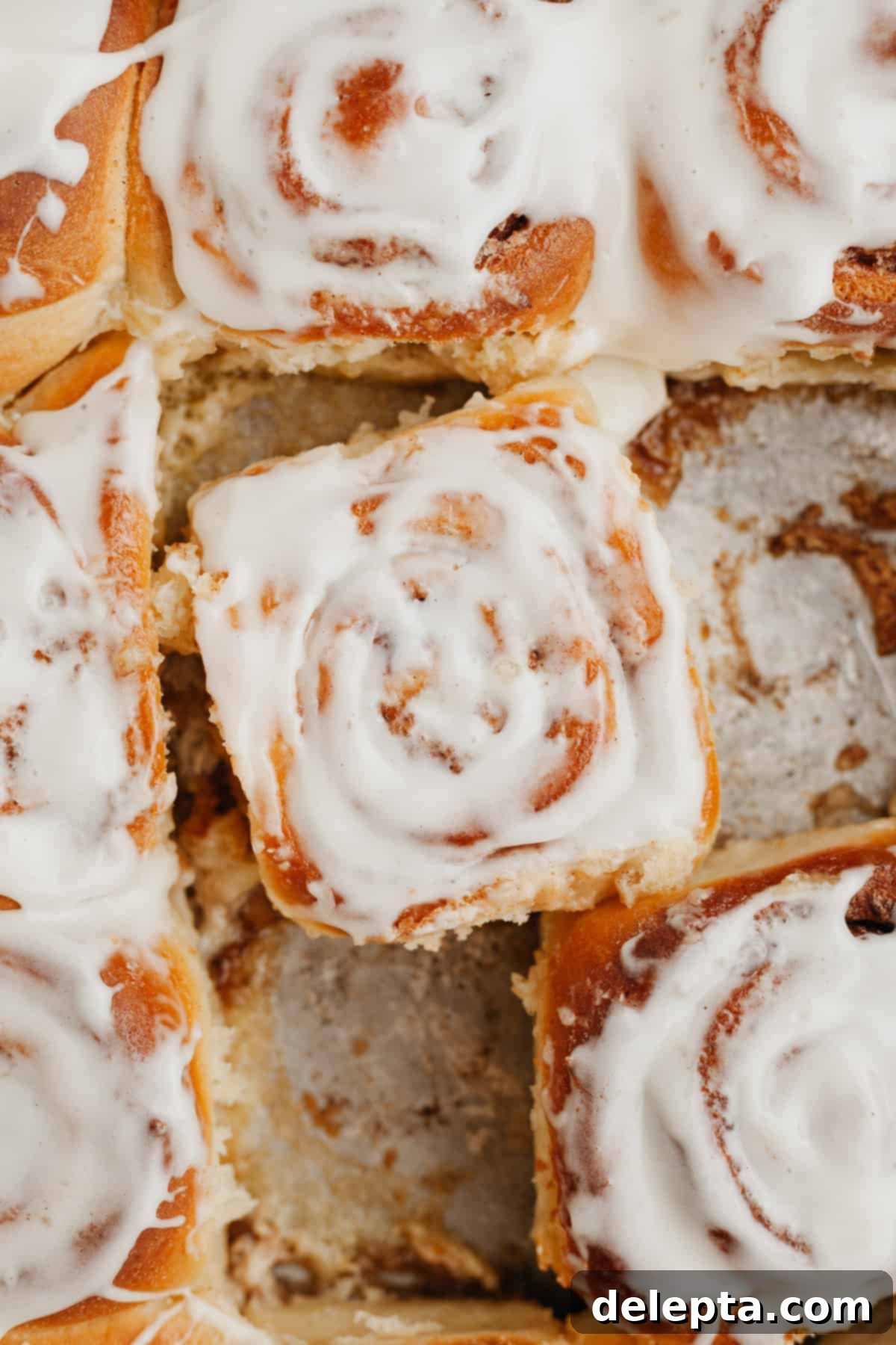 Decadent Brioche Cinnamon Rolls with Heavy Cream 2 Golden brown brioche cinnamon rolls baked in a pan, glistening under a generous layer of creamy white cream cheese frosting.