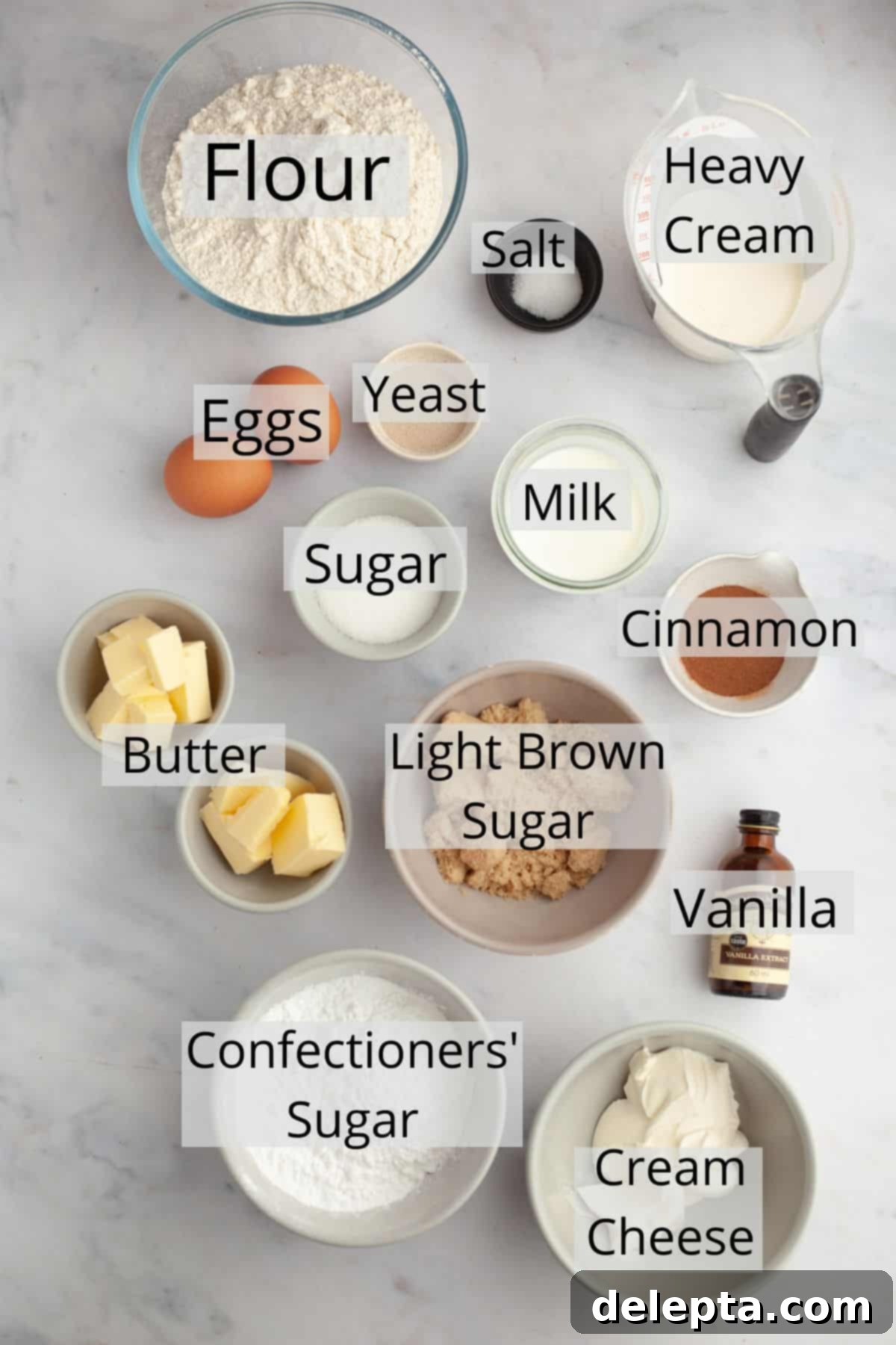 Decadent Brioche Cinnamon Rolls with Heavy Cream 3 A flat lay of various ingredients for brioche cinnamon rolls, including butter, eggs, milk, flour, sugar, and cream cheese.