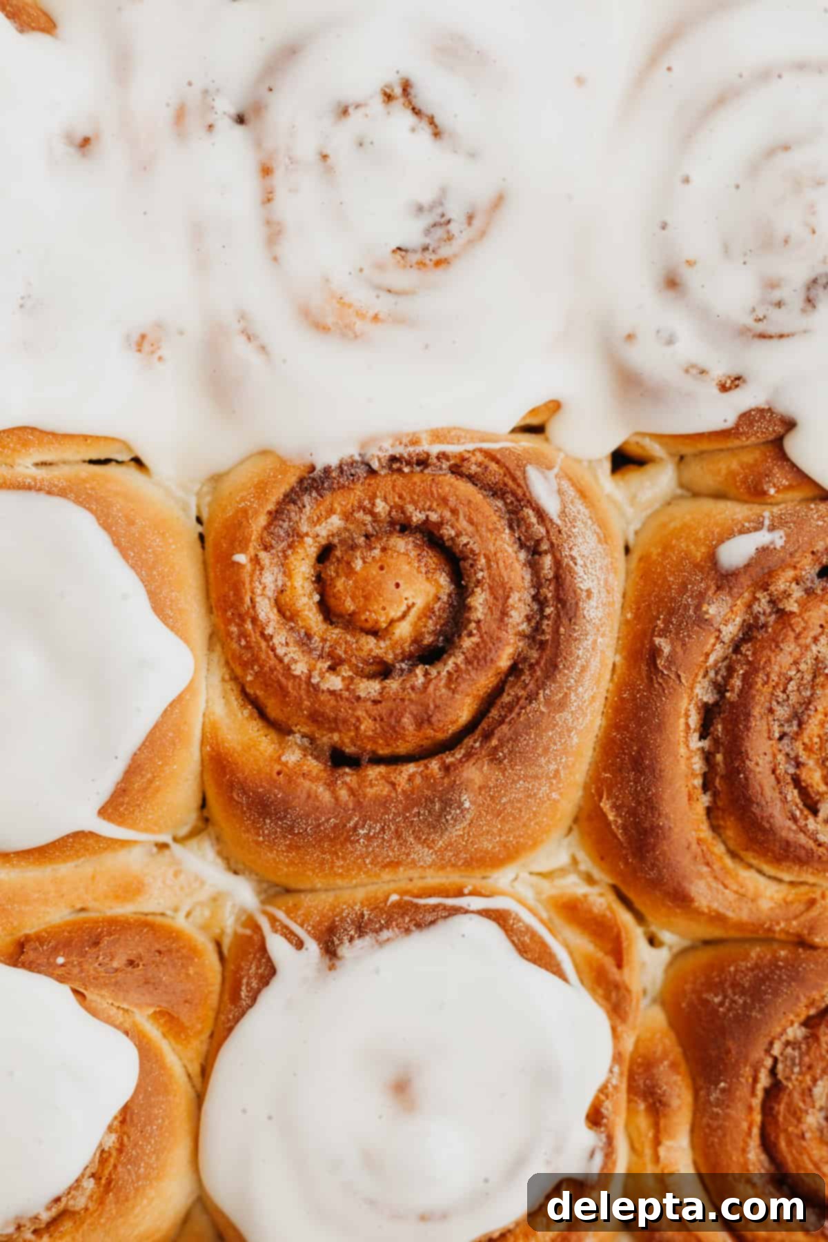 Decadent Brioche Cinnamon Rolls with Heavy Cream 9 A close-up of a pan of brioche cinnamon rolls, some partially covered in cream cheese glaze, highlighting their fluffy texture.