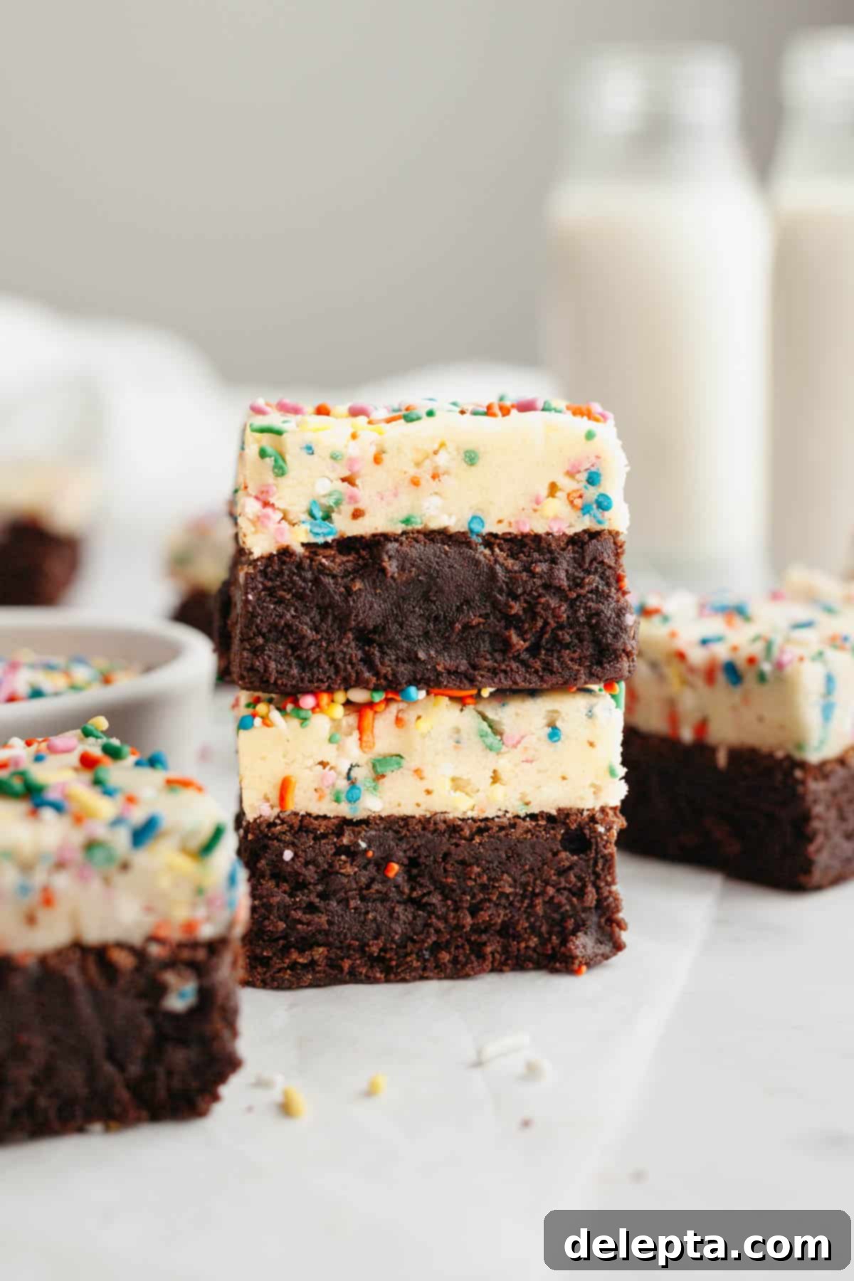 Funfetti Dream Brownies 8 A stack of two brownies on parchment paper. The brownies have a layer of rainbow sprinkle cookie dough on top.