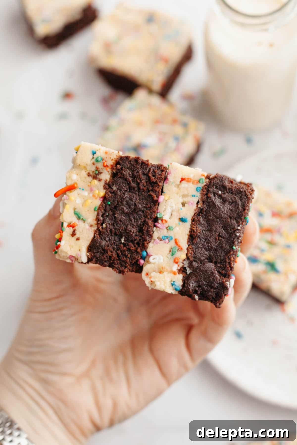 Funfetti Dream Brownies 9 A hand holding two brownies that have a layer of rainbow sprinkle cookie dough.