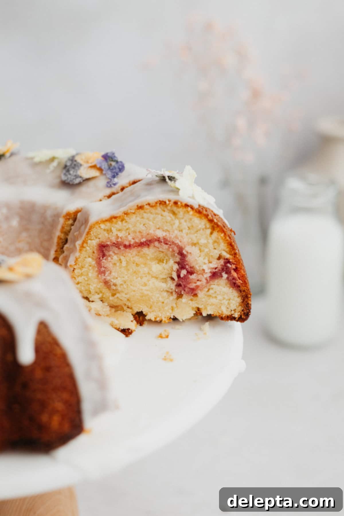 White Chocolate Raspberry Bundt Dream 2 A close up of a slice of bundt cake covered in a white glaze with a raspberry swirl.