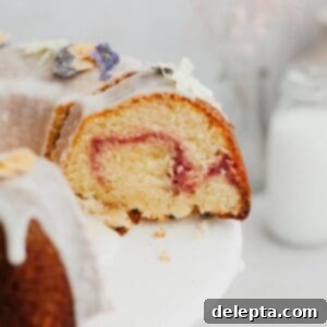 White Chocolate Raspberry Bundt Dream 9 A close up of a slice of bundt cake covered in a white glaze with a raspberry swirl.