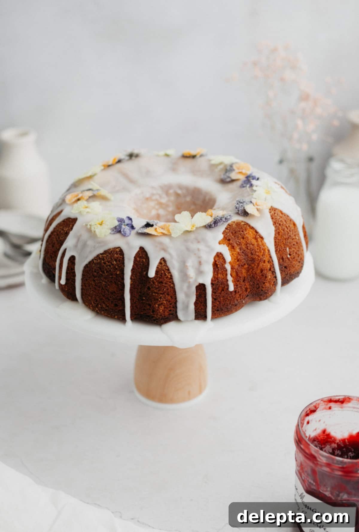 White Chocolate Raspberry Bundt Dream 7 A bundt cake with white icing on it on a white cake stand.