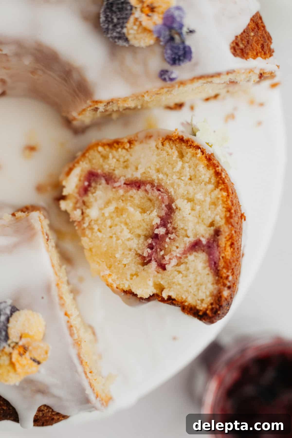 White Chocolate Raspberry Bundt Dream 8 A close up of a slice of bundt cake covered in a white glaze with a raspberry swirl.