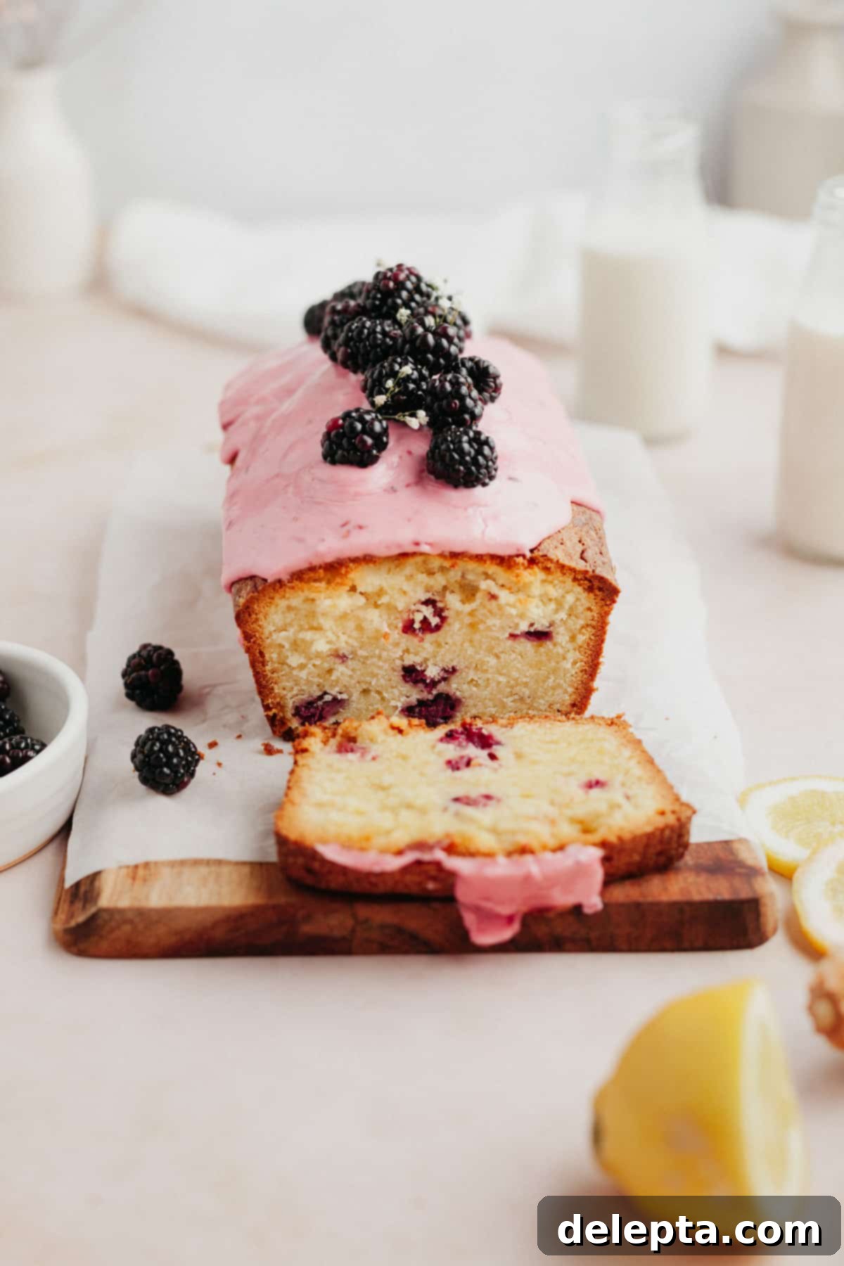Vibrant Blackberry Lemon Loaf 2 A perfectly sliced blackberry lemon loaf, showcasing its moist crumb, pink glaze, and fresh blackberries on top.