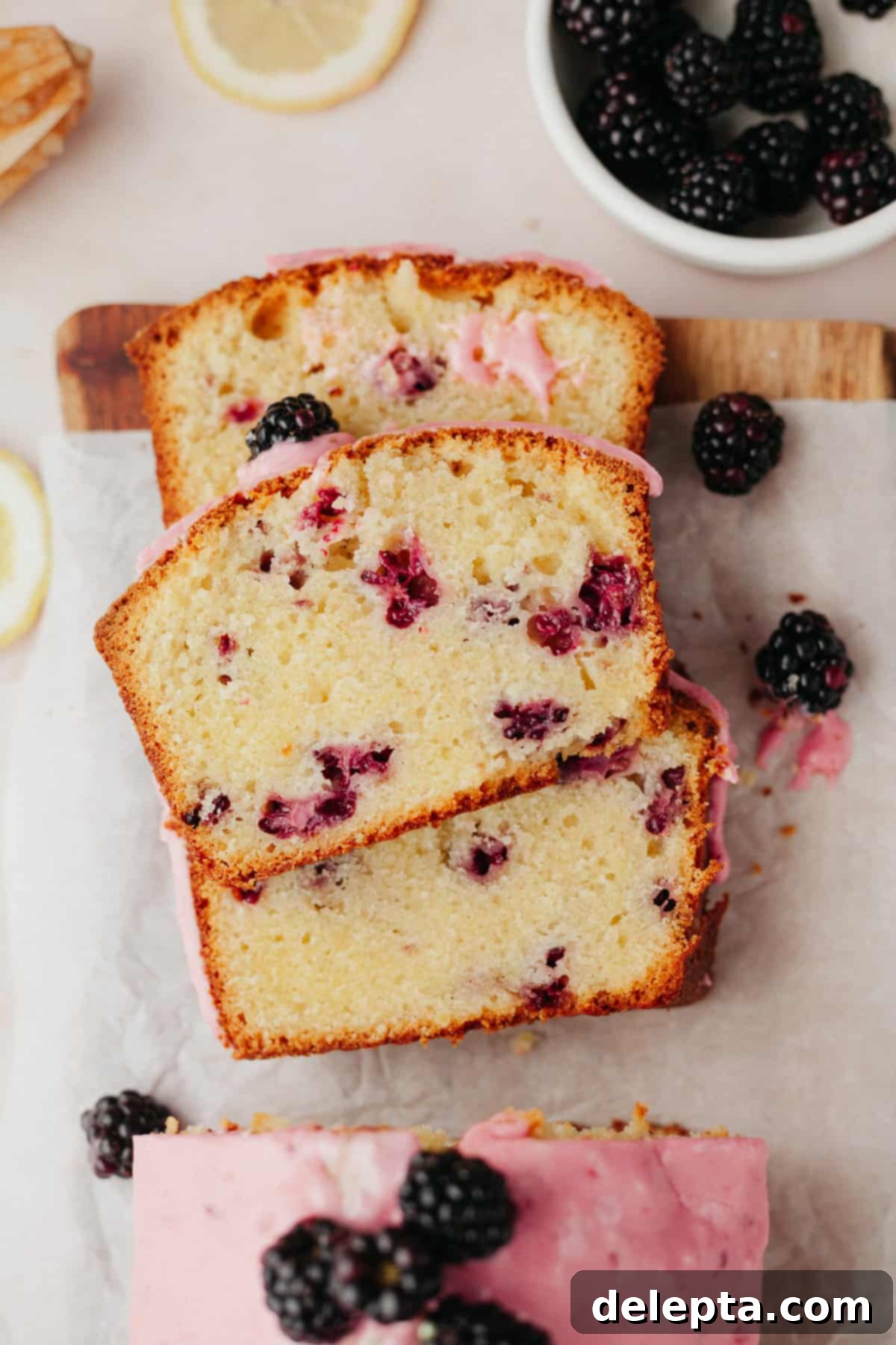 Vibrant Blackberry Lemon Loaf 8 Three perfectly stacked slices of sweet lemony bread with fresh blackberries and glaze, resting on parchment paper.